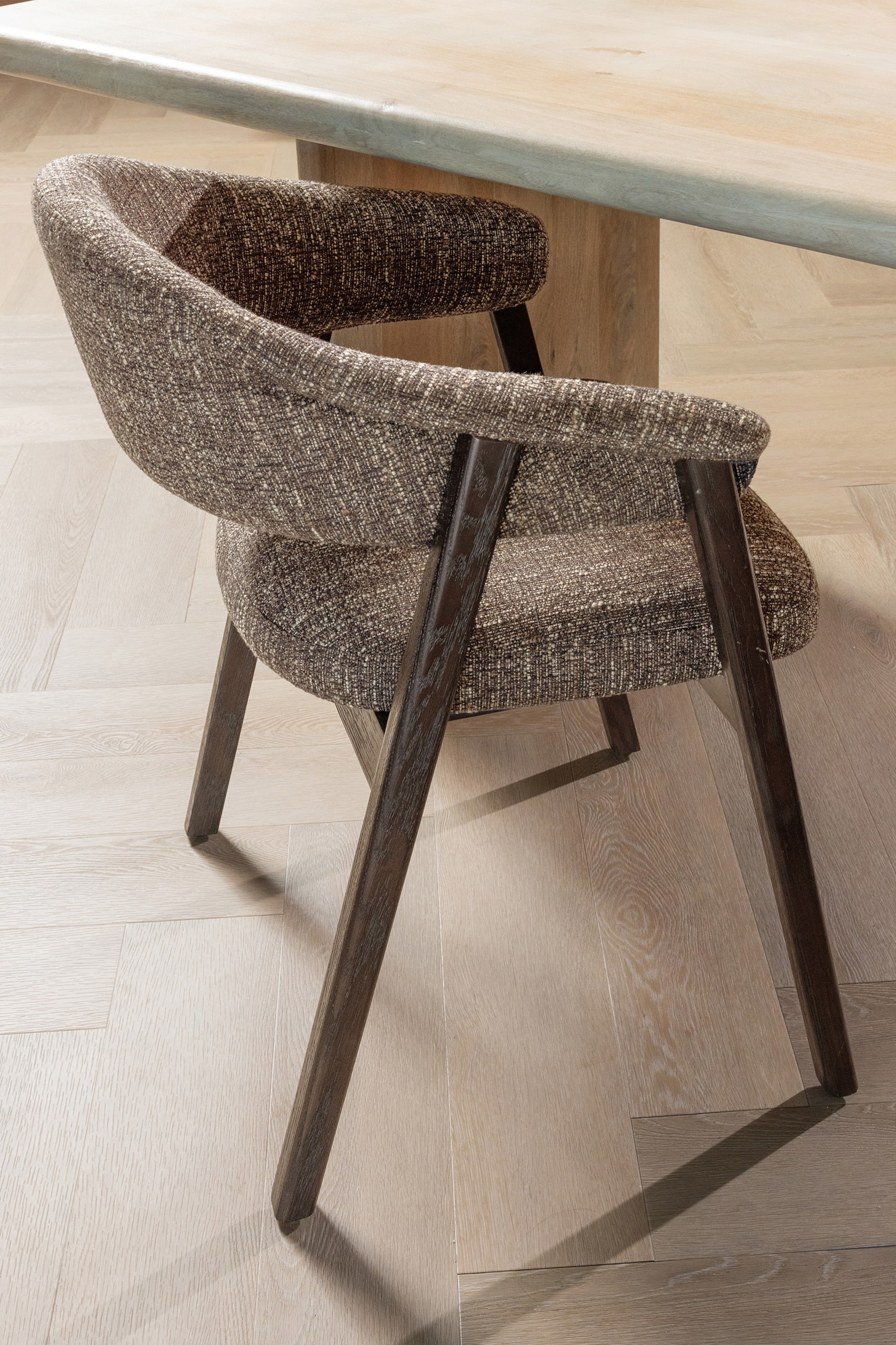 Agrandir l'image: Une chaise présente un dossier et une assise incurvés, recouverts d'un tissu texturé marron et gris. Des pieds en bois foncé soutiennent l'assise rembourrée et les accoudoirs intégrés, qui s'incurvent depuis le dossier, tandis que la chaise est inclinée pour présenter son côté et son dos.