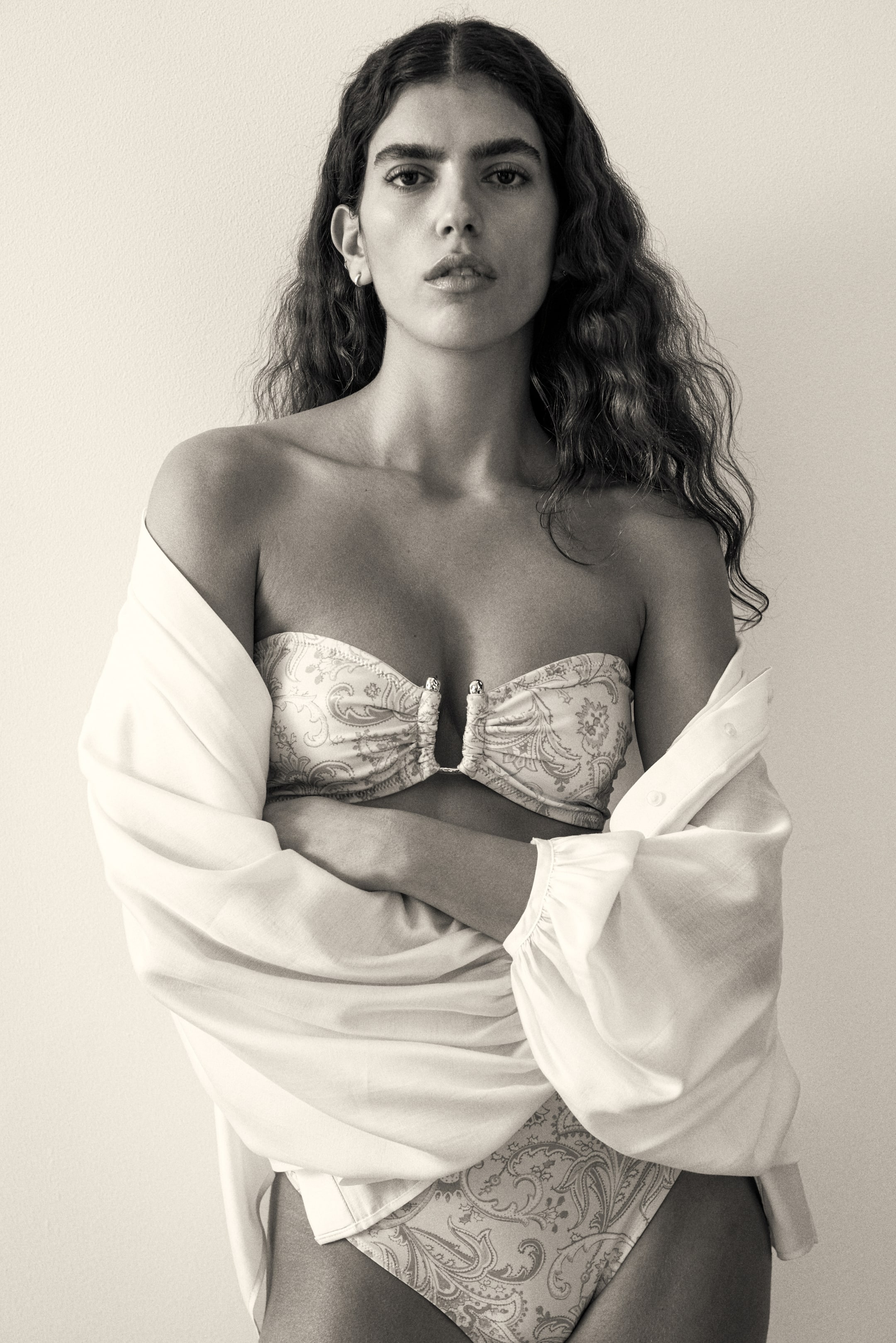 Ver imagen más grande: Se lleva un conjunto de bikini con estampado paisley en tonos claros, que consta de un top bandeau con centro fruncido y herraje en forma de U, y unas braguitas de corte alto a juego. Encima, se superpone abierta una camisa oversize de tonos claros con puños fruncidos.