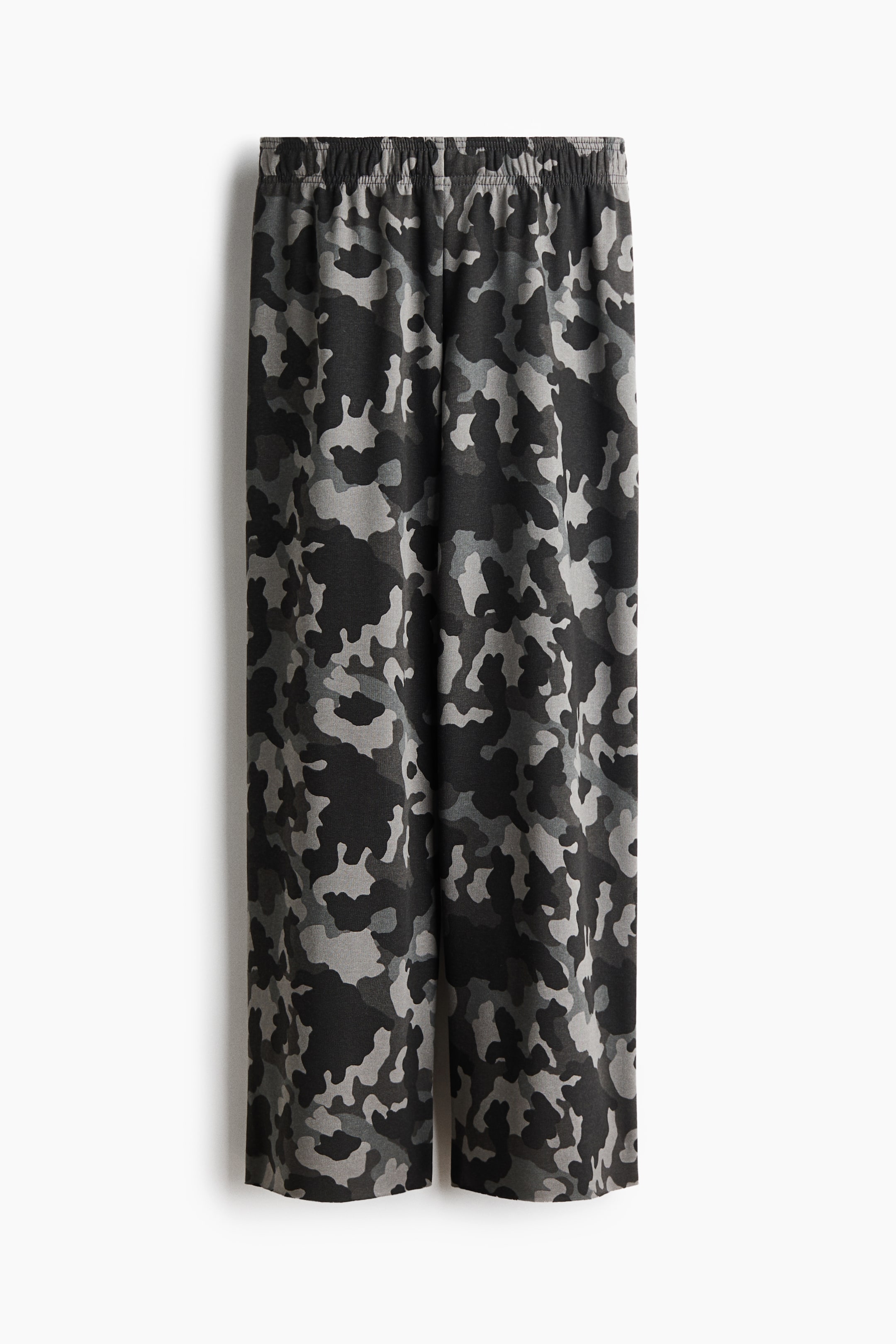 View larger image: These wide-leg pants feature a grey and black camouflage pattern, shown from the front. The design showcases a gathered elastic waistband and a relaxed, straight-leg cut.
