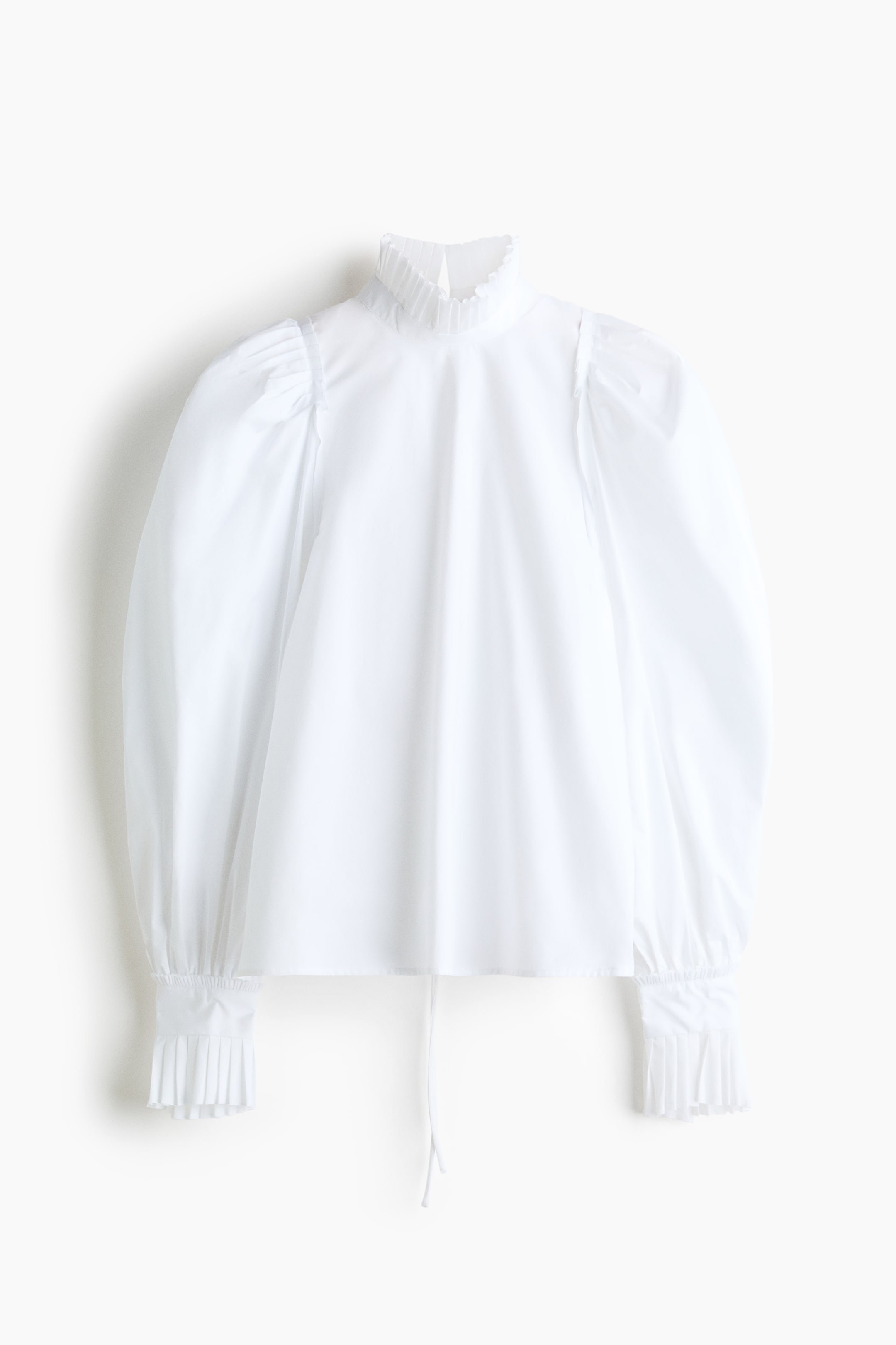 Ver imagen más grande: Se presenta una blusa blanca, con cuello alto tipo Mao con volantes y voluminosas mangas abullonadas. Las mangas fruncen en los hombros y terminan en largos puños plisados, y se aprecia un cordón ajustable en el bajo.