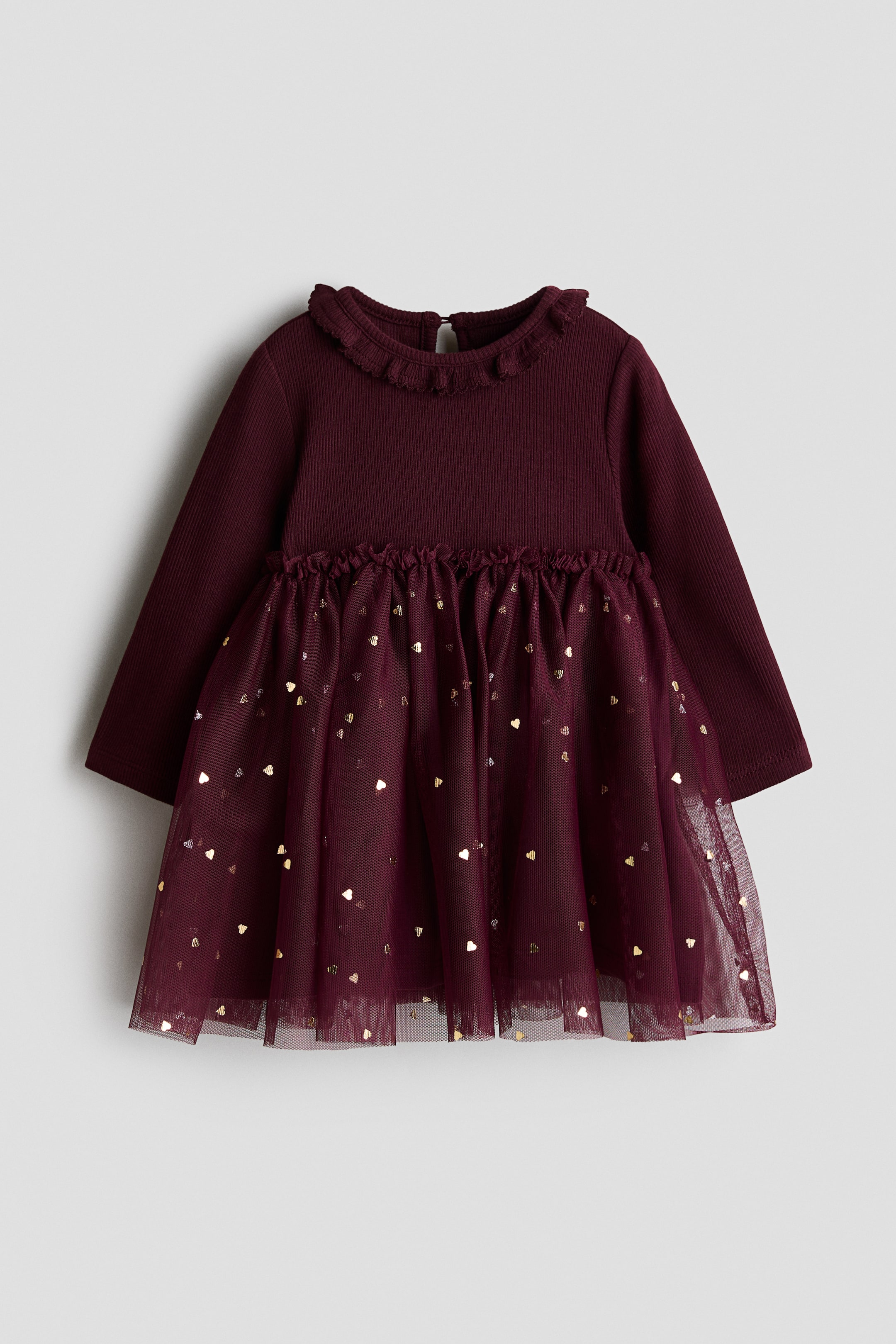 View larger image: A long-sleeved burgundy dress is facing front, featuring a ribbed top with a round, frill-trimmed neckline and a visible keyhole opening with a button at the back. A narrow frill trim separates the top from the flared tulle skirt, which is decorated with small gold hearts.