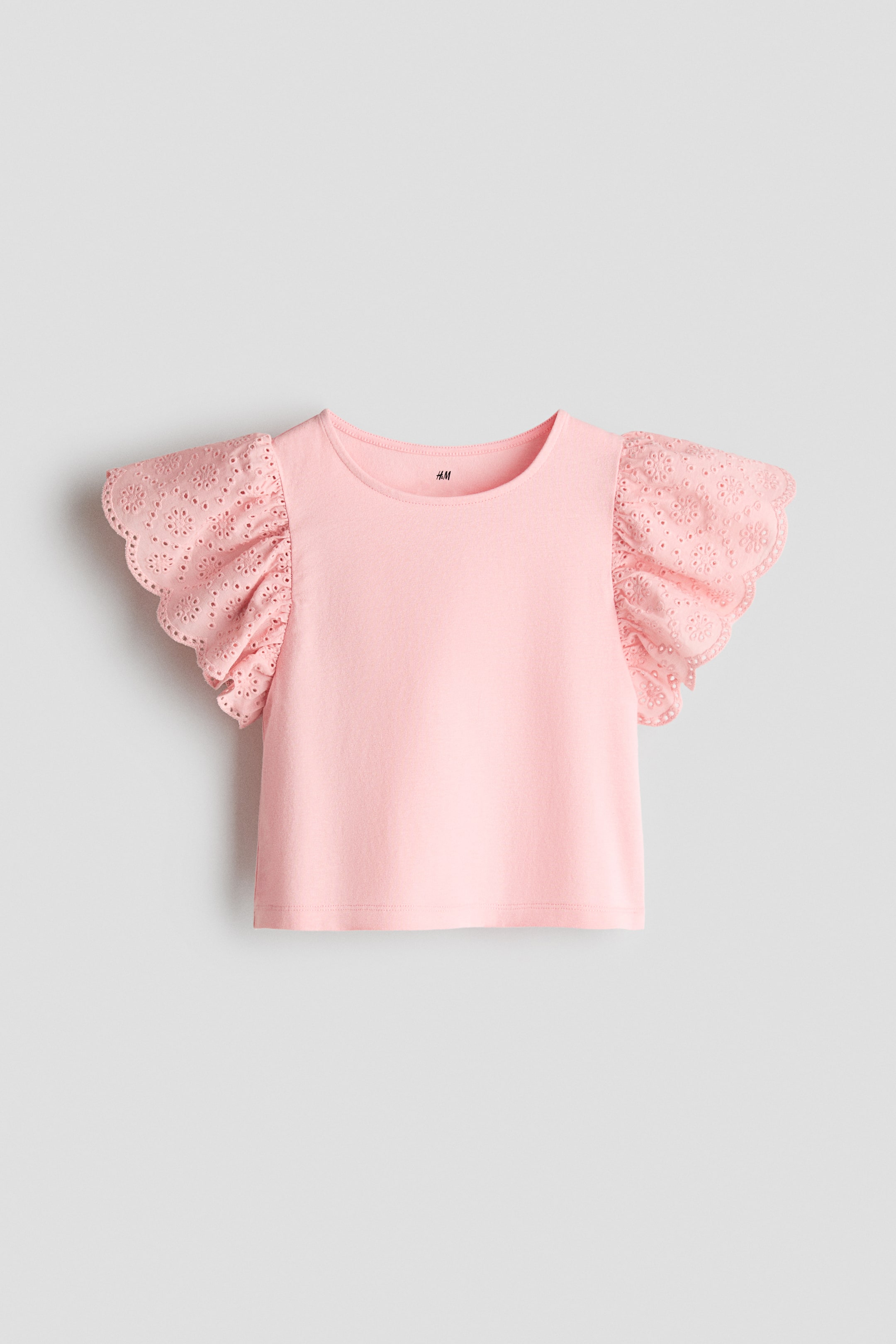 Ampliar la imagen: Un top rosa que presenta un escote redondo y mangas con volantes, presentado de FRENTE. El cuerpo está hecho de suave jersey de algodón, mientras que las mangas están confeccionadas con un tejido de algodón con bordado inglés y bordes festoneados.