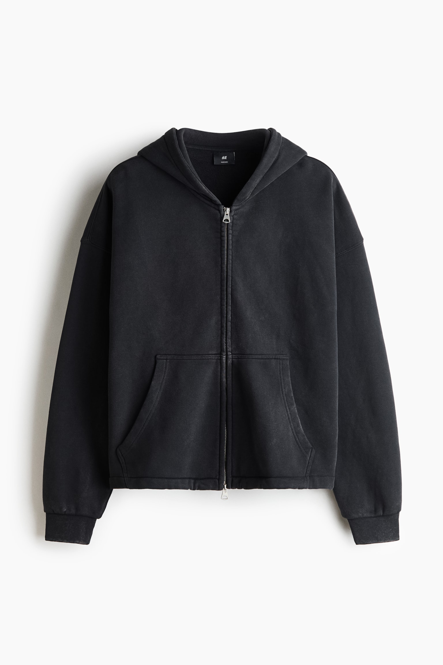 This boxy-style, washed black zip-through hoodie is shown from the front, featuring a jersey-lined hood, dropped shoulders, and long sleeves with ribbed cuffs. It showcases a two-way front zip and split kangaroo pockets, highlighting its oversized, baggy silhouette.