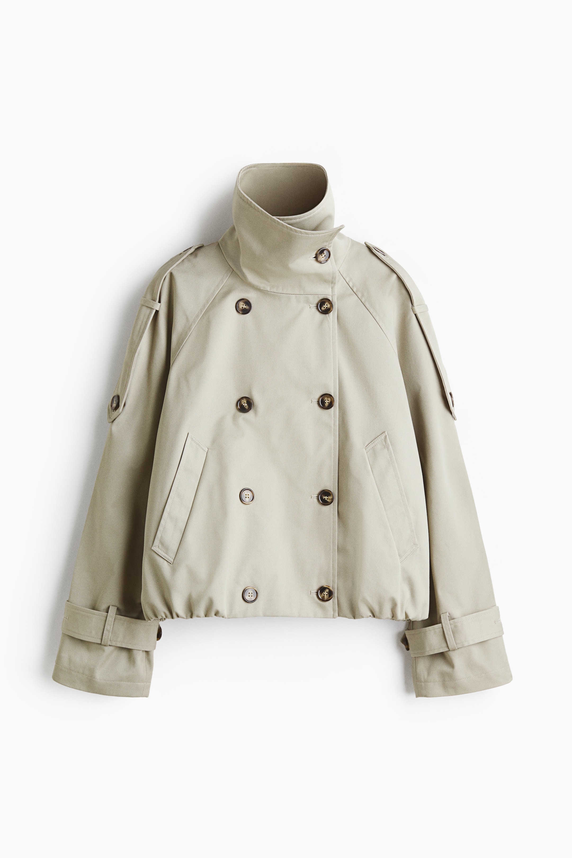 View larger image: A short, oversized twill trench coat is showcased from the front, featuring a high collar and a double-breasted button front with buttoned epaulettes. It is designed with raglan sleeves and tab and button cuffs, welt front pockets, a bubble hem creating a puffy silhouette, and is lined.