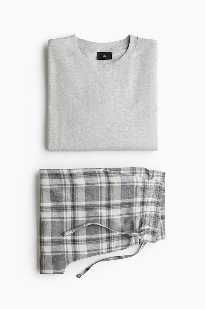 Ett pyjamasset visas vikt platt och bestÃ¥r av en ljusgrÃ¥ topp i bomullsjersey med rund halsringning samt ett par rutiga flanellbyxor i grÃ¥tt, vitt och beige med synlig dragsko i midjan. - 1