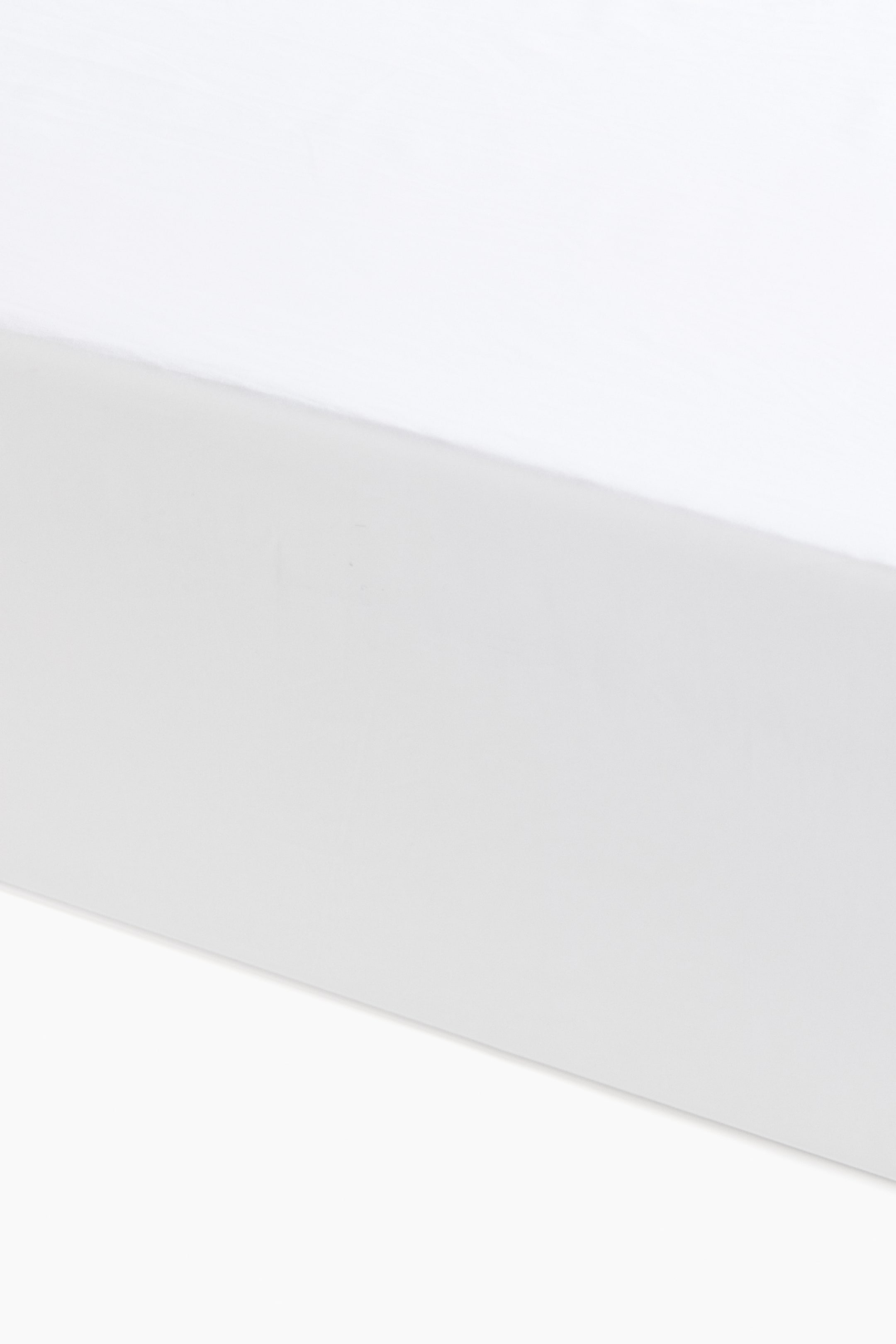 Voir une image plus grande: Un drap-housse blanc présente sa surface supérieure lisse et plate ainsi qu'une partie de son côté avant. Le tissu en percale de coton à fils fins et tissage serré exhibe une texture douce et soyeuse.