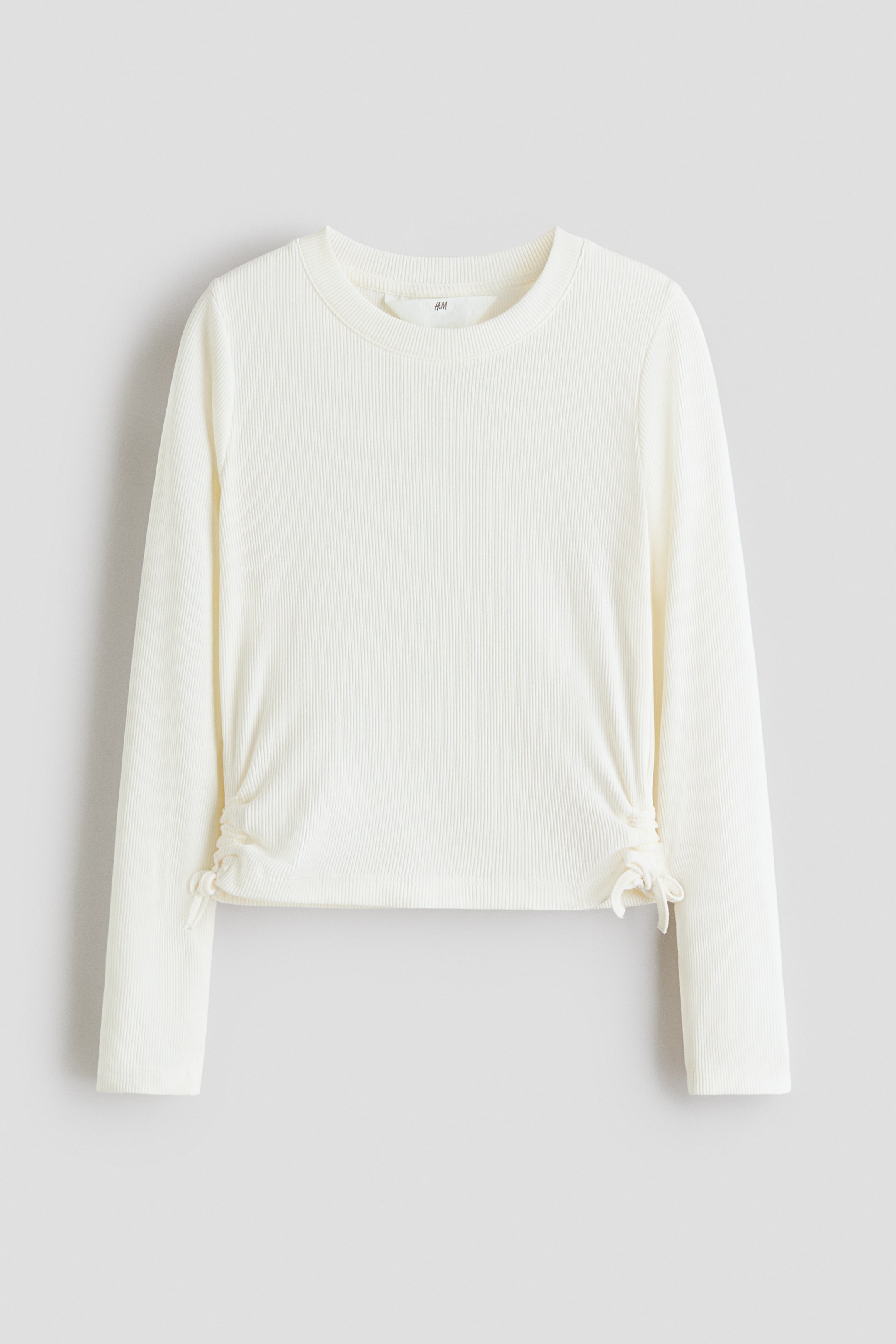View larger image: A cream ribbed long-sleeve top showcasing a crew neck with adjustable ruched detailing and ties on both side seams at the hem.