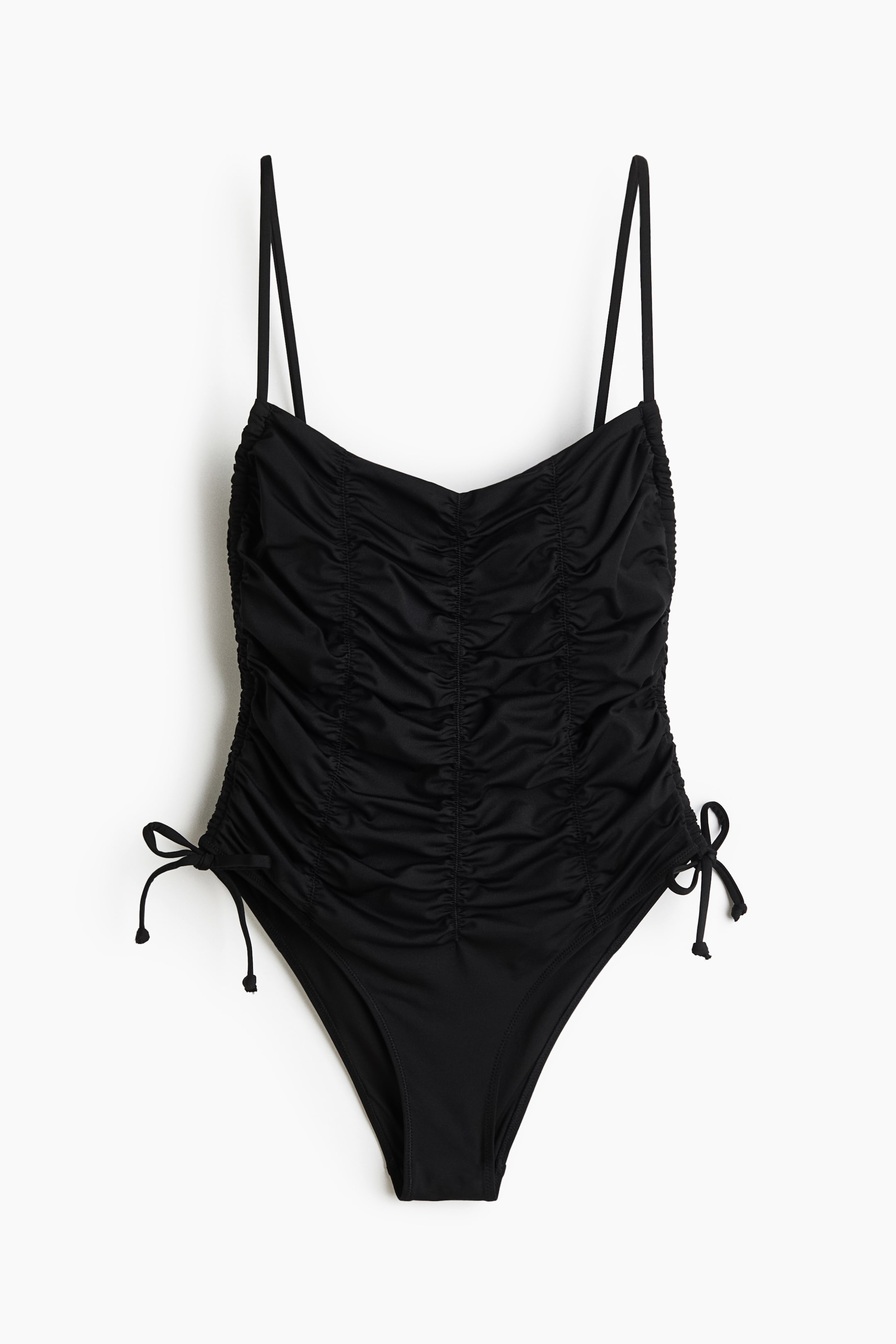 Ver imagen más grande: Se muestra un bañador negro de una pieza visto de frente, con tirantes finos estilo espagueti y un escote curvo. Presenta un fruncido pronunciado en el torso y cordones ajustables anudados en las caderas formando lazos.