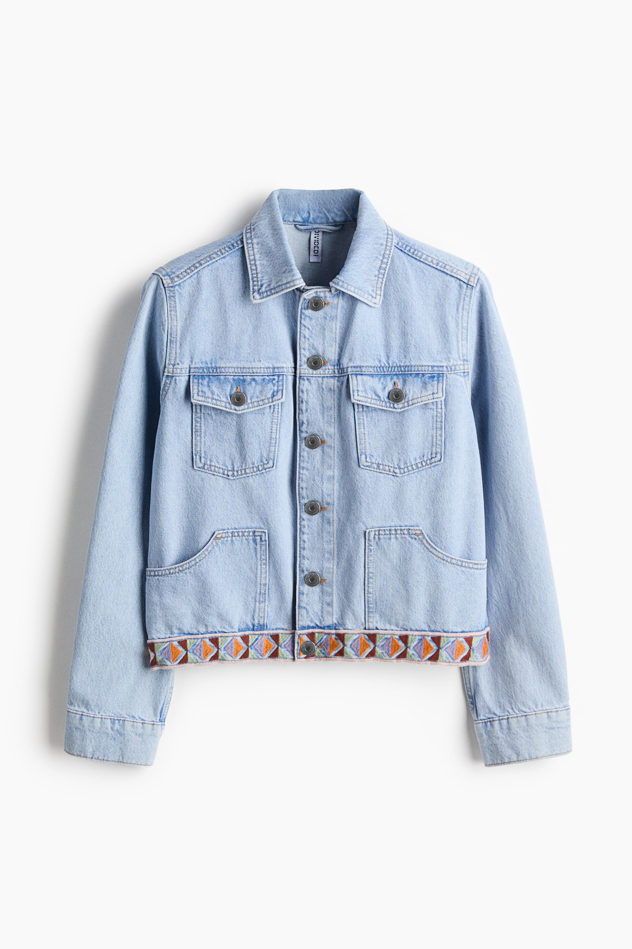 Visualizza immagine più grande: Una giacca di jeans azzurro chiaro è presentata di FRONTE, con un colletto a punta, una chiusura frontale con bottoni in metallo e due tasche sul petto con pattina e chiusura a bottoni in metallo. Due grandi tasche a toppa sono visibili in vita, mentre una fascia geometrica ricamata nei colori arancione, viola, verde e marrone decora l'orlo inferiore.
