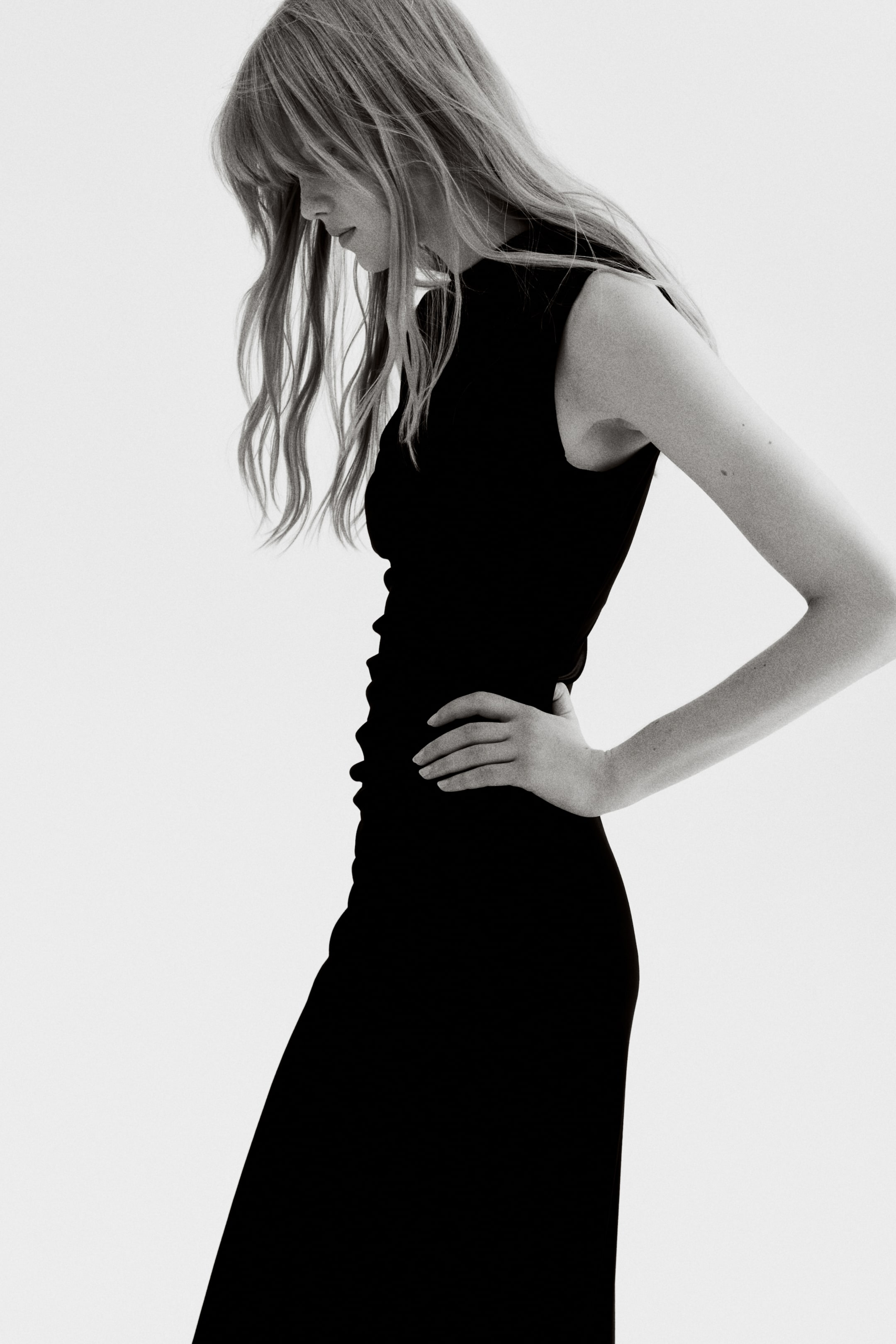 View larger image: A fitted, black, sleeveless maxi dress, featuring a turtle neck and a draped effect at the waist from pleats, is being worn by the model. The model is posing with her hand on her hip.
