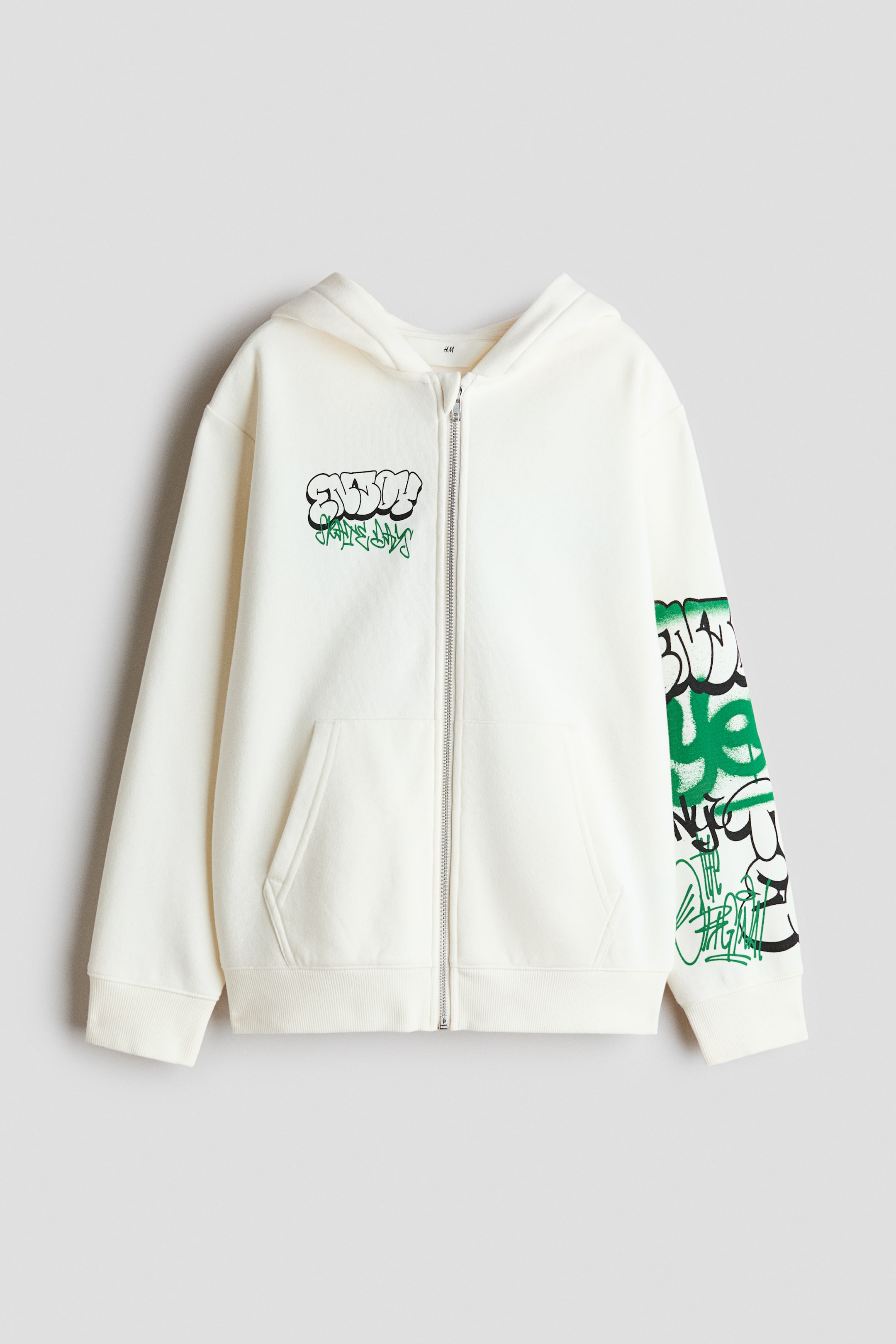 Visa större bild: FRAM: En krämfärgad zip-genom hoodie med graffiti-stil motiv i grönt och svart på framsidan och vänster ärm. Den är designad med en dragkedja i full längd, en huva, nedhasade axlar, framfickor och ribbade muddar och fåll.