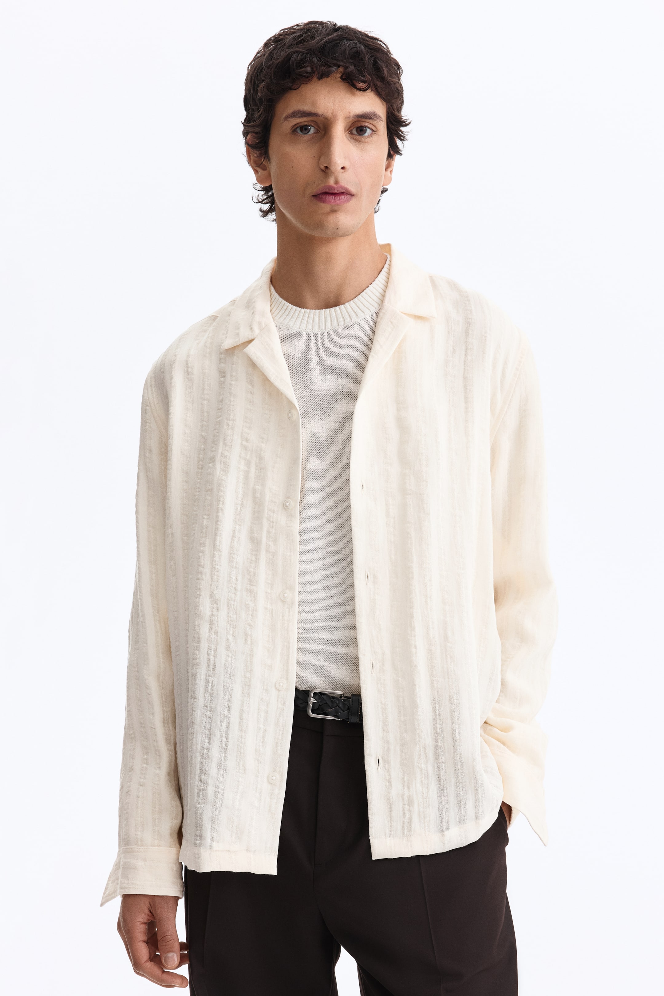 View larger image: A light beige button-front shirt is worn open over a cream sweater. It features a camp collar, long sleeves with button cuffs, and vertical textured stripes throughout.