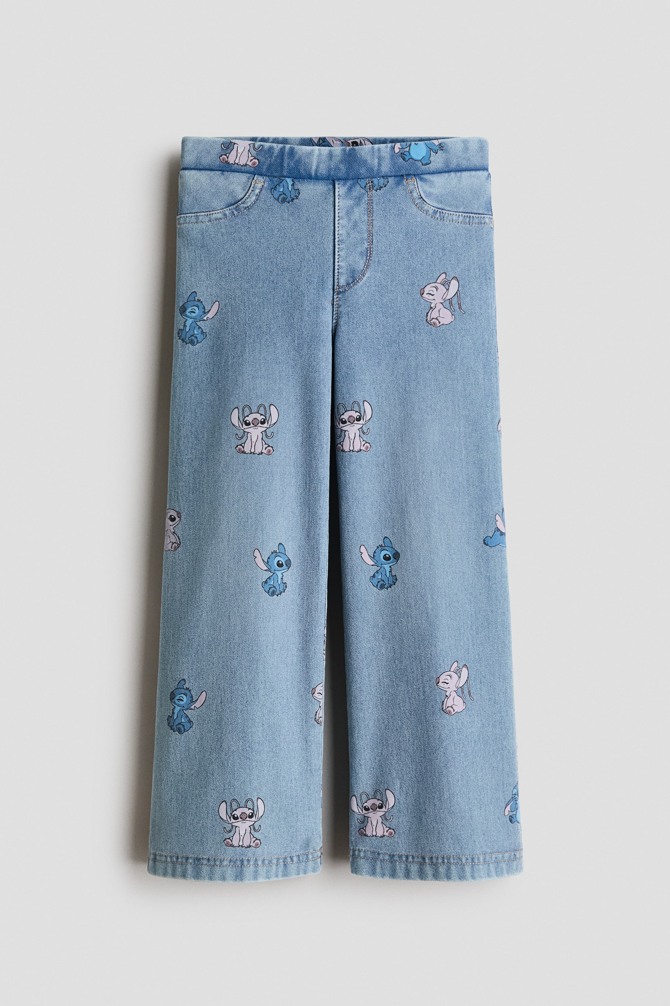Voir une image plus grande: Ces jeggings en jersey effet denim, bleu pâle, présentent une coupe à jambe large vue de face, avec un imprimé intégral de motifs de personnages de dessin animé bleus et roses. Le modèle comprend une taille élastiquée, une braguette factice et des surpiqûres décoratives aux poches avant.