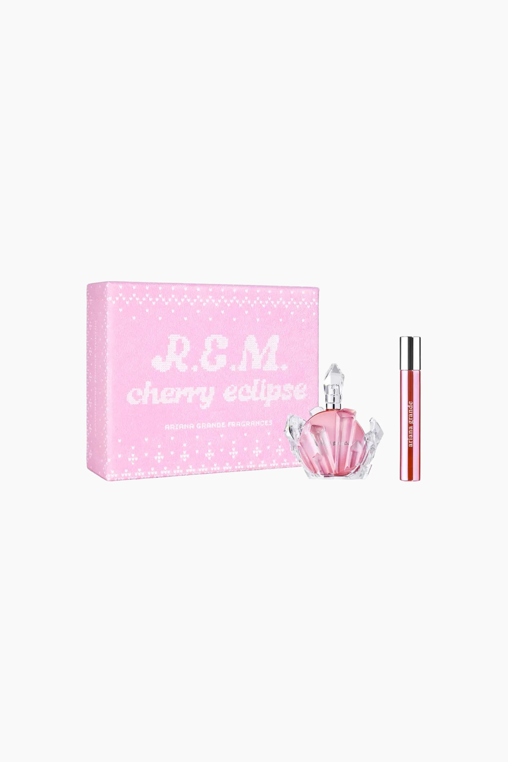 Se større billede: R.e.m. Cherry Eclipse Edp gavesættet viser en pink rektangulær gaveæske vinklet en smule mod venstre med et hvidt strikket-lignende mønster og branding. Ved siden af æsken står en rund pink parfume flaske, der hviler i en gennemsigtig, multifacetteret krystal-lignende holder, samt en slank pink rejsespray med sølvfarvet låg.