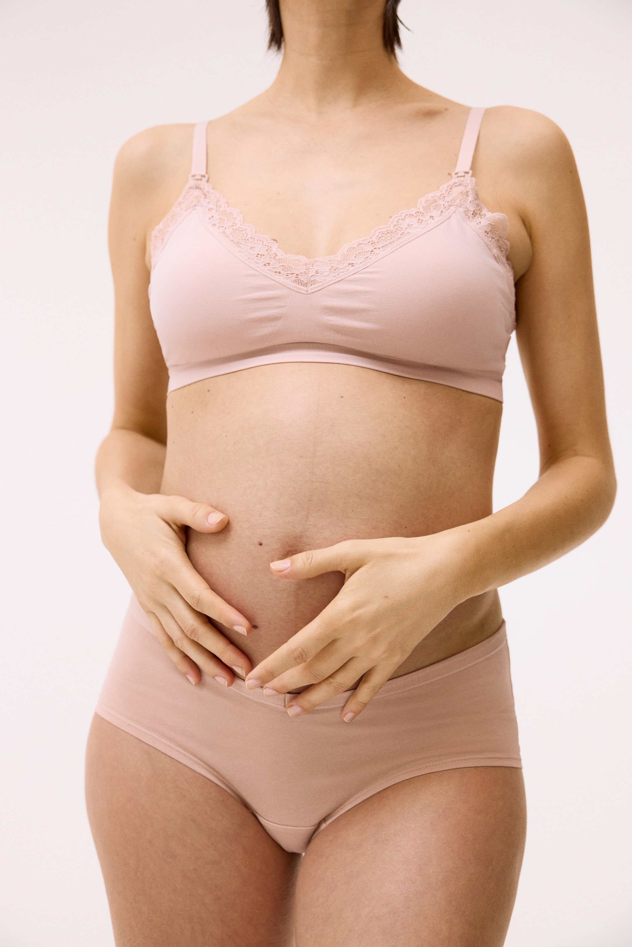 Agrandir l'image: Un soutien-gorge d'allaitement rose clair avec une bordure en dentelle le long de l'encolure en V et des attaches d'allaitement sur les bretelles est porté. Un slip assorti rose clair avec une taille en V à l'avant est également porté.
