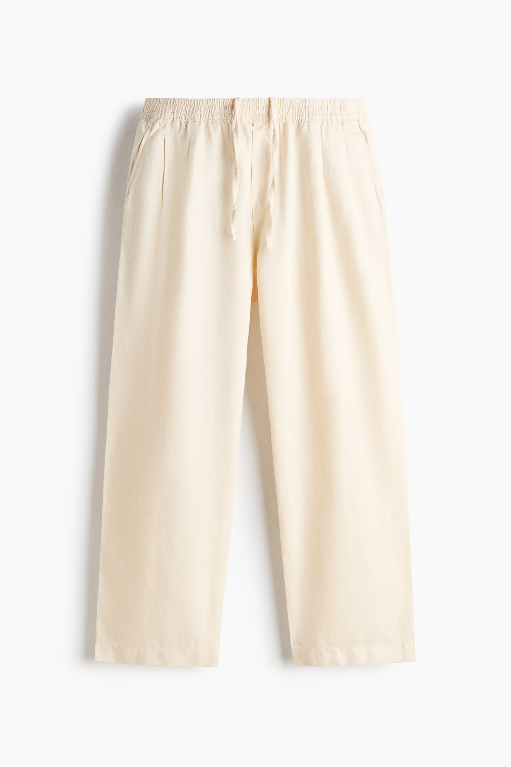 View larger image: These cream-coloured trousers are shown from the front, featuring an elasticated waistband with a drawstring and front pleats. The trousers are hanging with a relaxed fit and straight legs, showcasing a lightweight, textured fabric.