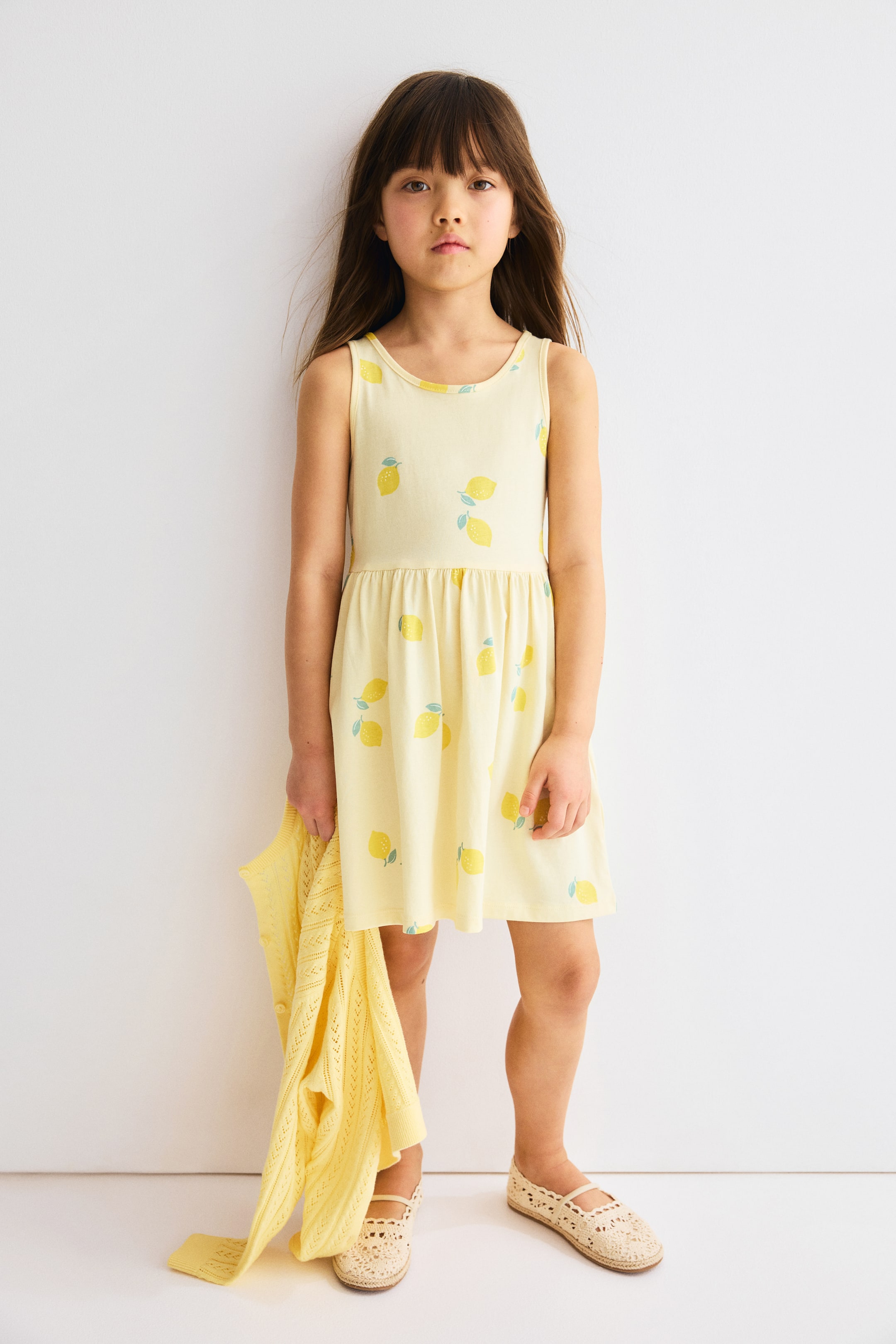 Größeres Bild ansehen: Ein hellgelbes ärmelloses Kleid mit Rundhalsausschnitt, geraffter Taille und einem durchgehenden Zitronenmuster im Stoff.