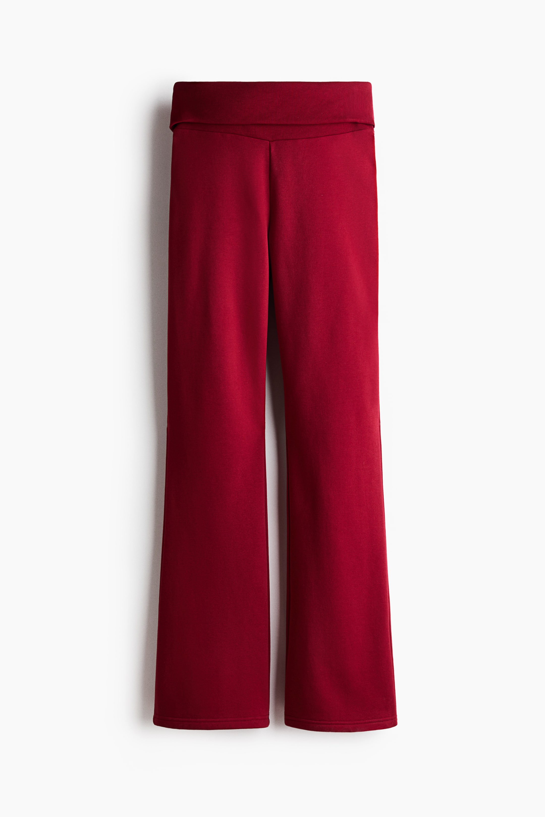 Größeres Bild anzeigen: Ein Paar tiefrote Wide-Leg-Hosen ist von vorne zu sehen, mit einem breiten, umgeschlagenen Bund und einer lässigen Passform, die zum Saum hin leicht ausgestellt ist. Die Hose besteht aus einem glatten, weich wirkenden Strickstoff mit sauber verarbeiteten Säumen.