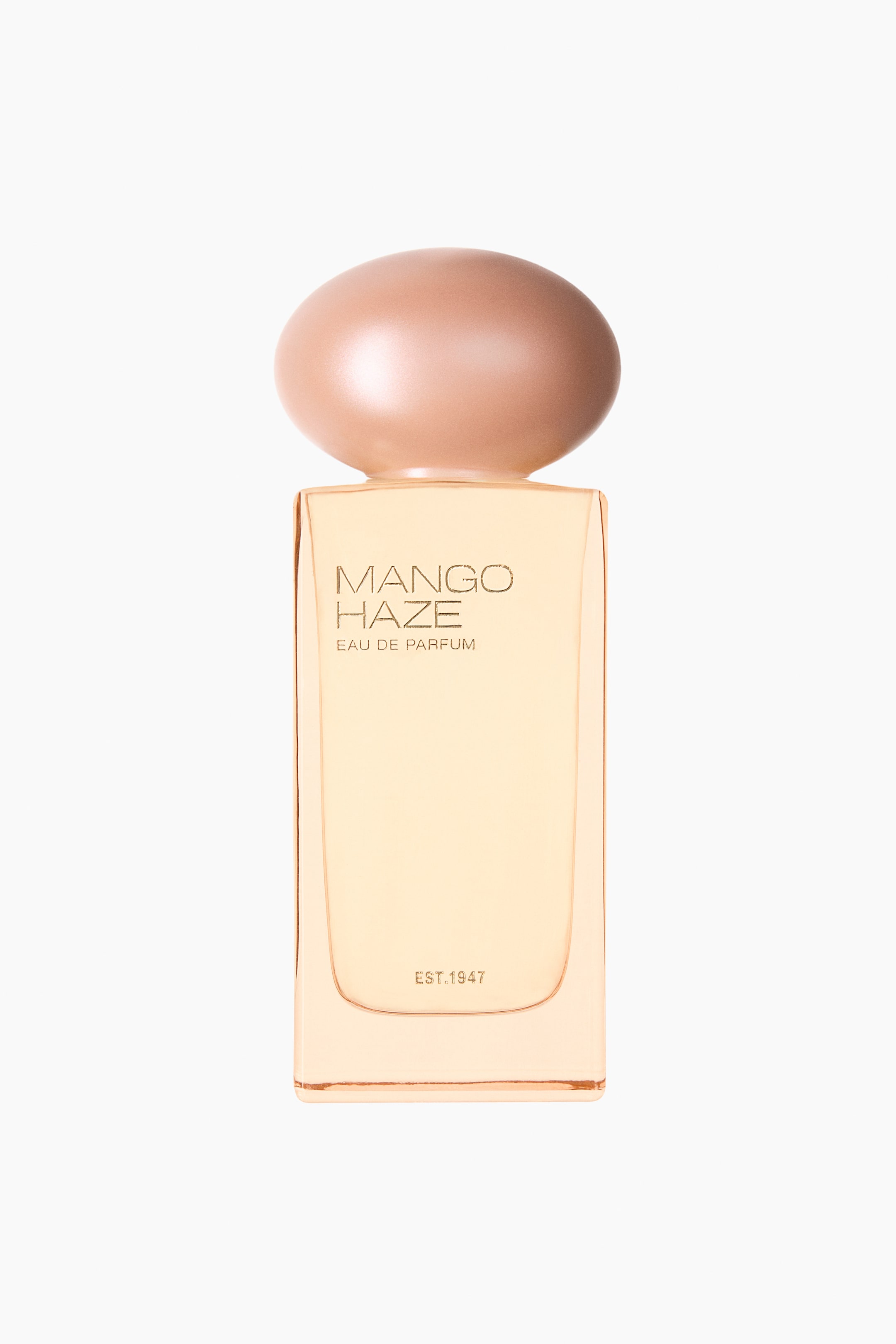 Vezi imaginea mai mare: Mango Haze EdP este prezentat într-o sticlă dreptunghiulară din sticlă transparentă, conținând un lichid chihlimbariu deschis, văzută din față. Sticla afișează inscripția „MANGO HAZE EAU DE PARFUM” cu litere aurii, iar dedesubt este vizibil „EST.1947”, fiind completată de un capac oval, sidefat, în nuanță deschisă de rose gold.