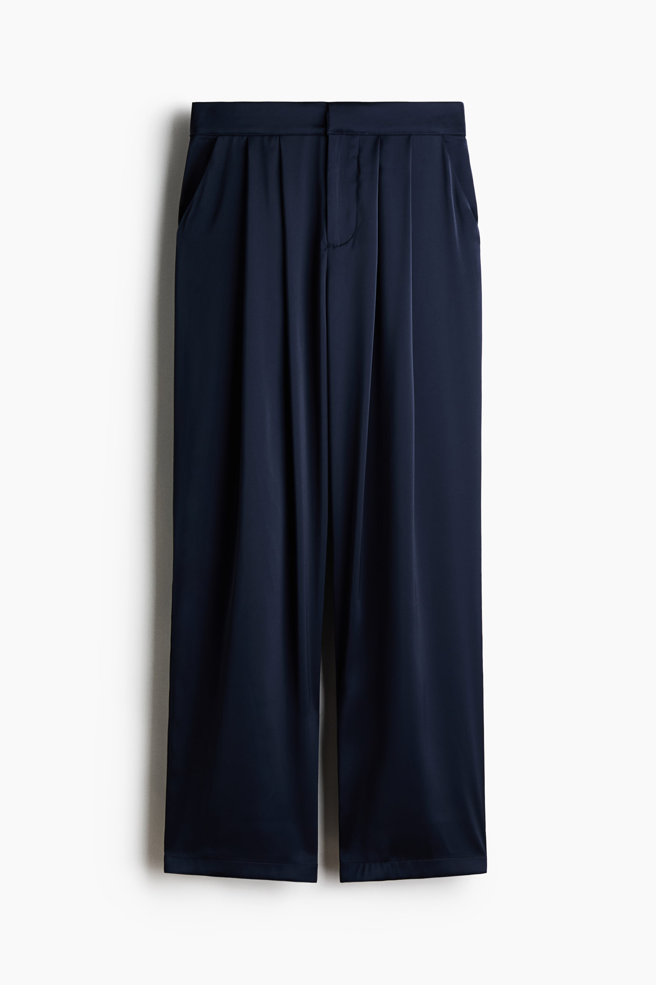 View larger image: A pair of navy blue wide-leg trousers is hanging front-facing, featuring a high-rise waistband with front pleating that creates a draped, relaxed fit. The trousers are showing a smooth, lustrous fabric with side slip pockets and a concealed front closure.