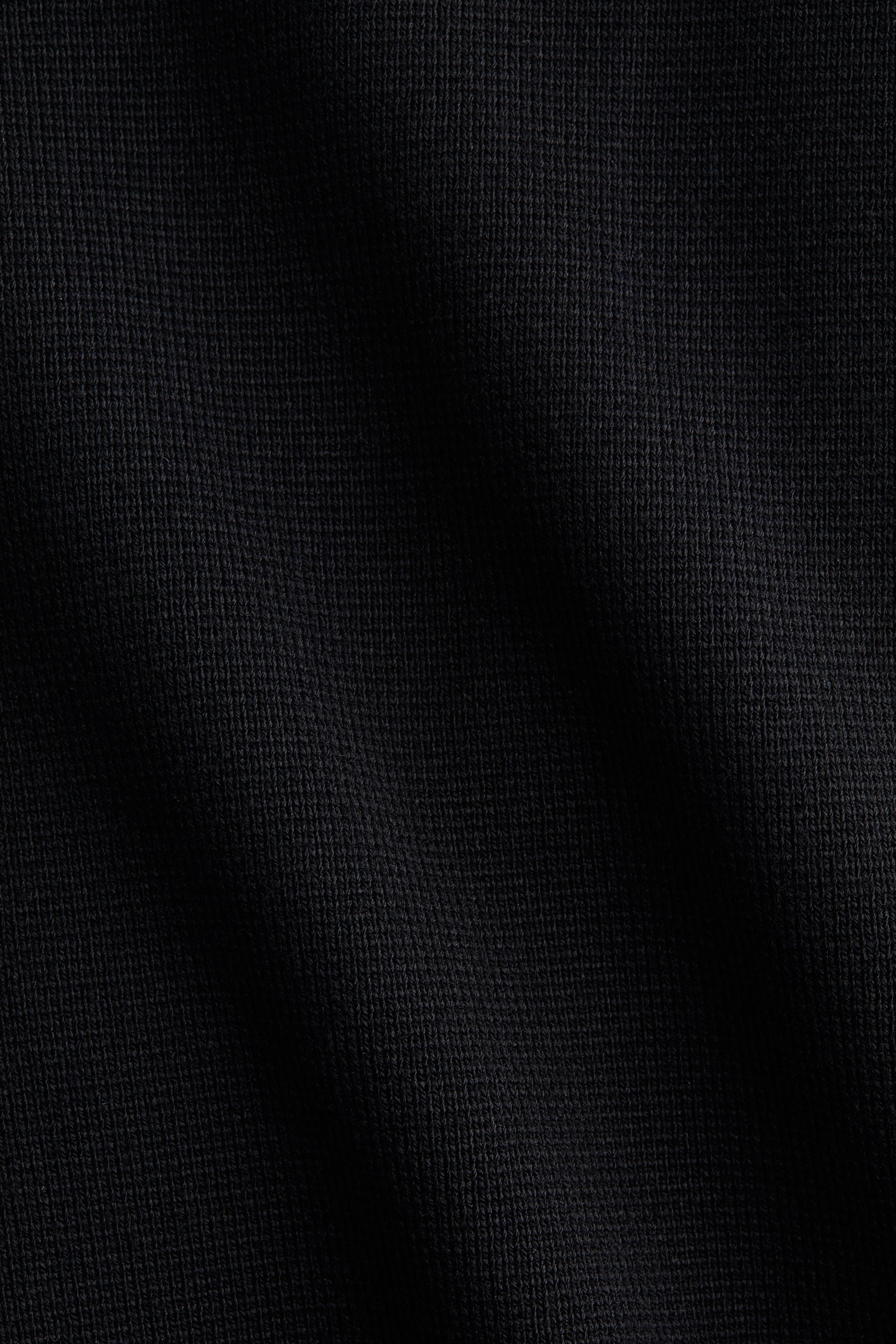 Büyük resmi görüntüle: Siyah bir örme kumaş, ince ve tutarlı bir örme yapısı sergiliyor, yüzeyinde hafif kıvrımlar ışık ve gölgede değişiklikler yaratarak çeşitlilik oluşturuyor.