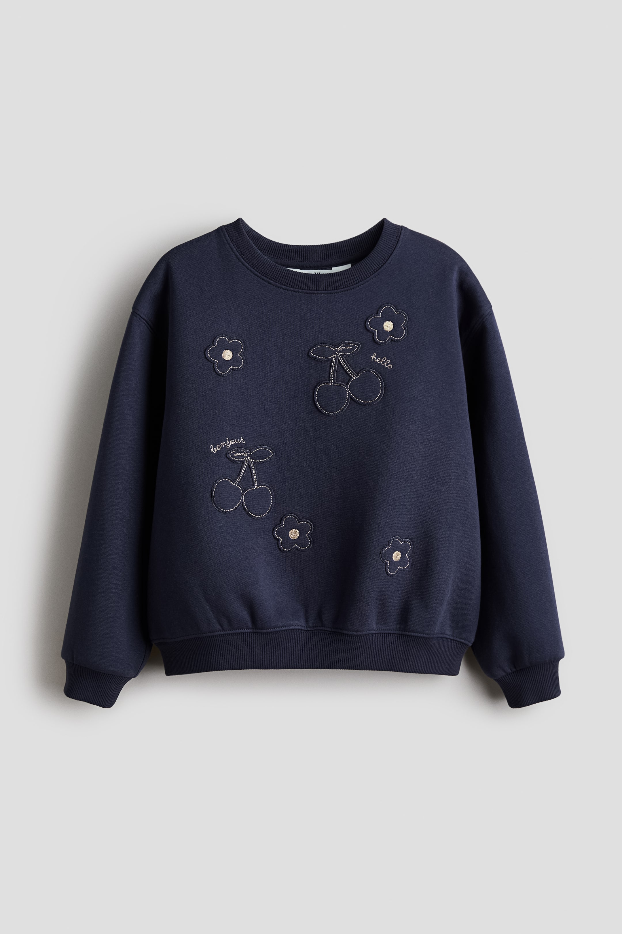 View larger image: A dark blue sweatshirt in sweatshirt fabric, shown from the FRONT, features a round, rib-trimmed neckline, dropped shoulders, and ribbed cuffs and hem. Its front is adorned with metallic-outlined cherry and flower appliqués, alongside embroidered "hello" and "bonjour" text.