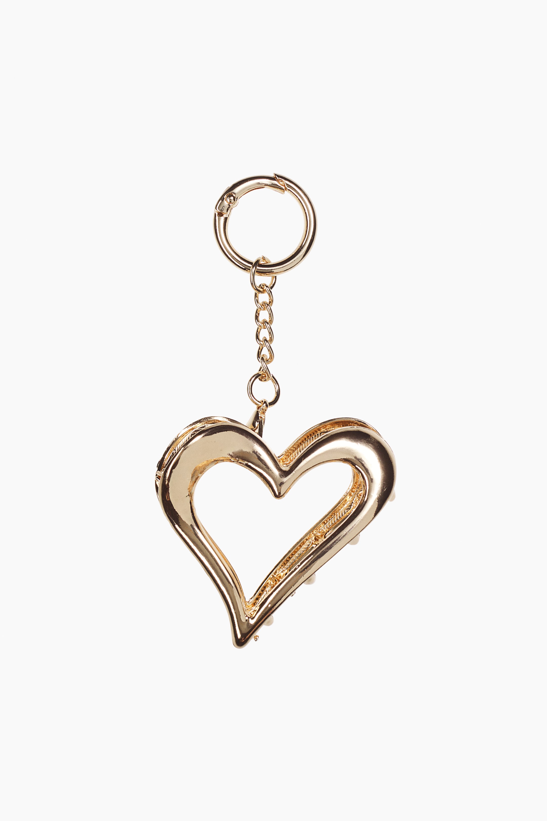 Größeres Bild anzeigen: Ein goldfarbenes Schlüsselanhänger-Accessoire hängt senkrecht und zeigt eine hohle, herzförmige Krallenklammer, die an einer kurzen Gliederkette und einem runden Federkarabiner befestigt ist. Die polierte Metallklammer ist frontal ausgerichtet und präsentiert ihre glatte, reflektierende Oberfläche sowie die dezent sichtbaren Krallezähne entlang der Innenkante.