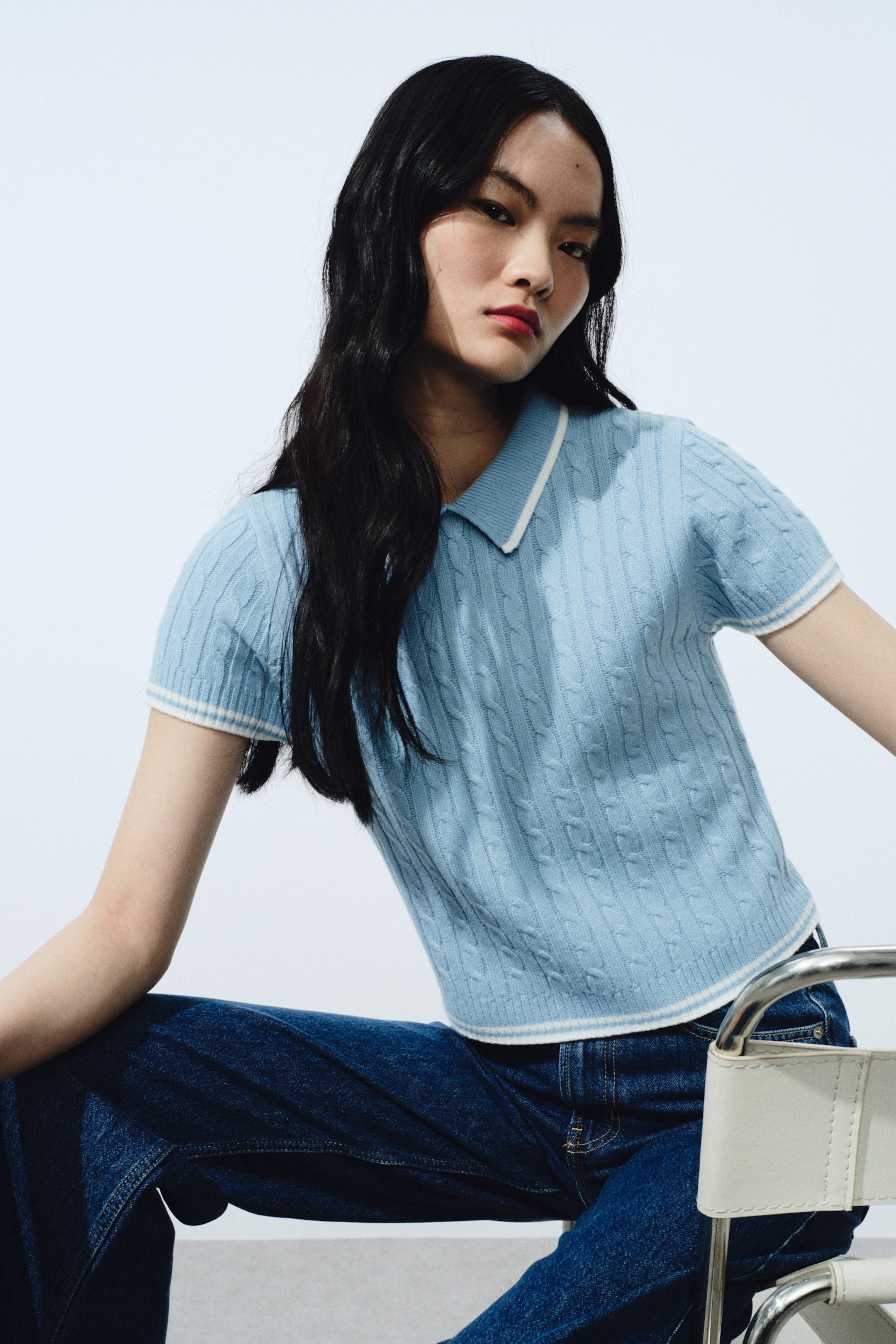 View larger image: A light-blue cable-knit polo top features a pointed collar trimmed in white. It is designed with short sleeves showcasing white-and-blue striped ribbed cuffs, and a matching striped ribbed hem rests just above the waistline.