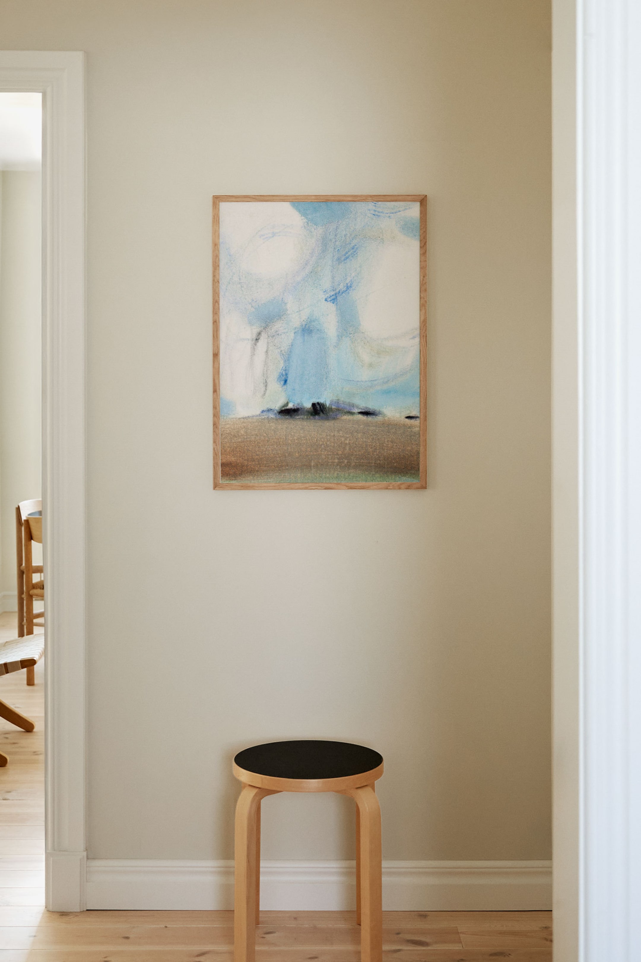 Visa större bild: En ljus träpall står i en lätt vinkel, dess tre böjda ben stöder en cirkulär svart sits.