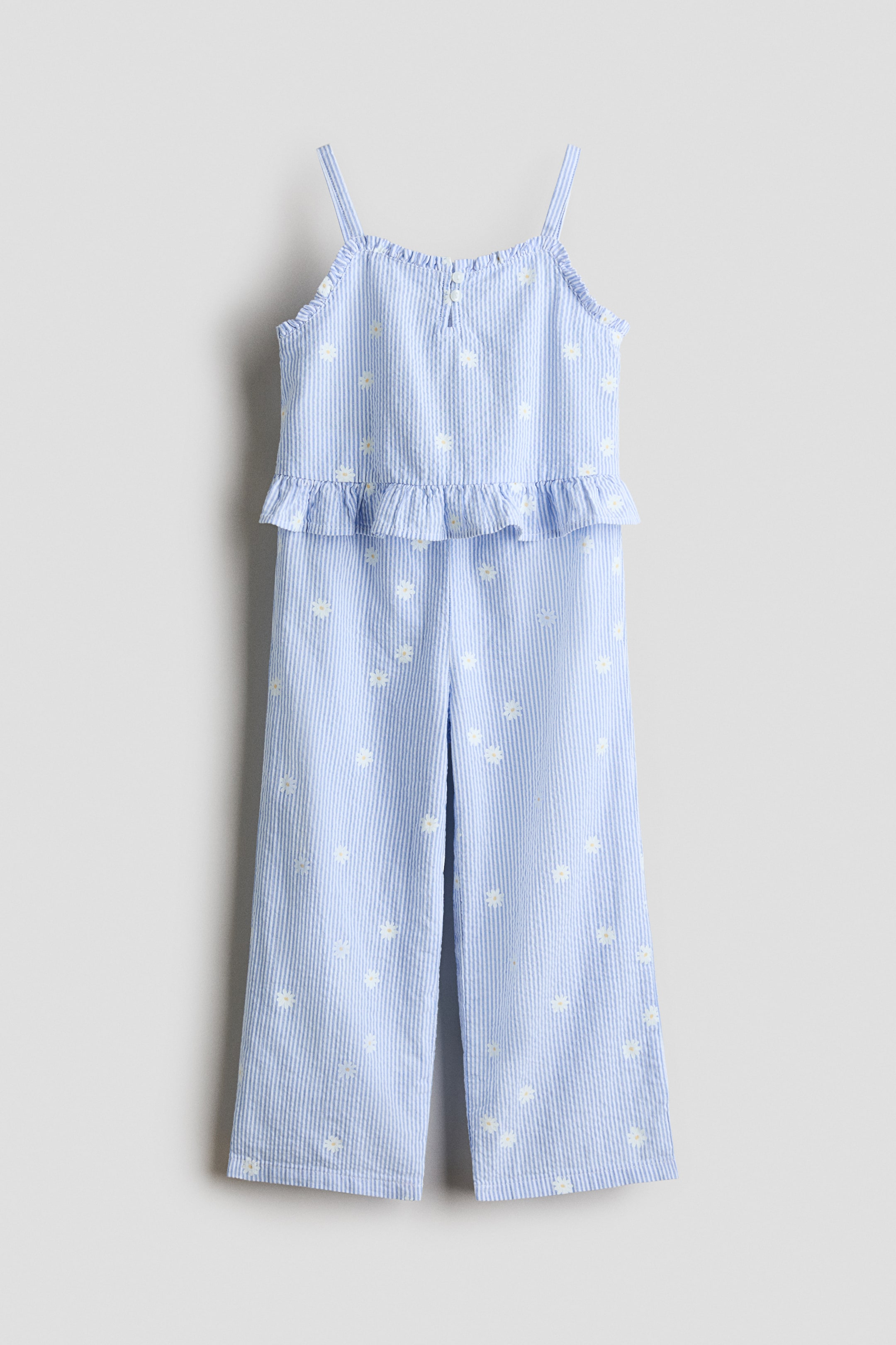 View larger image: A coordinating set, shown FRONT, features a top and pants in breezy cotton seersucker, adorned with light blue and white stripes and small white daisy-like flowers. The top includes narrow shoulder straps, a square neckline with a keyhole opening and buttons at the front, and frill trim around the top and hem. The pants are designed with an elasticated waist, wide legs, and frill-trimmed hems.