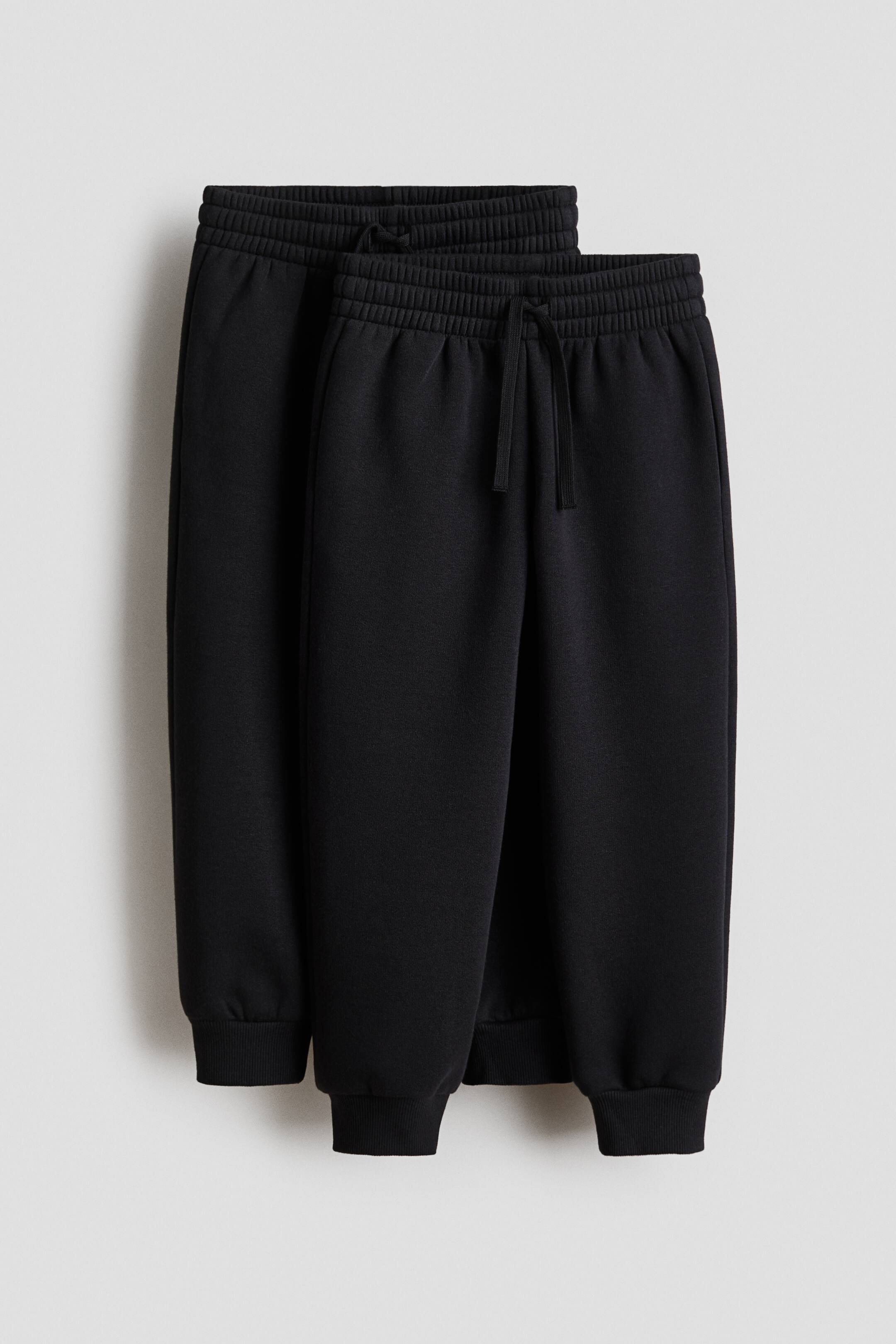 View larger image: Two pairs of black joggers are presented FRONT, featuring elasticated drawstring waists, side pockets and ribbed cuffs.