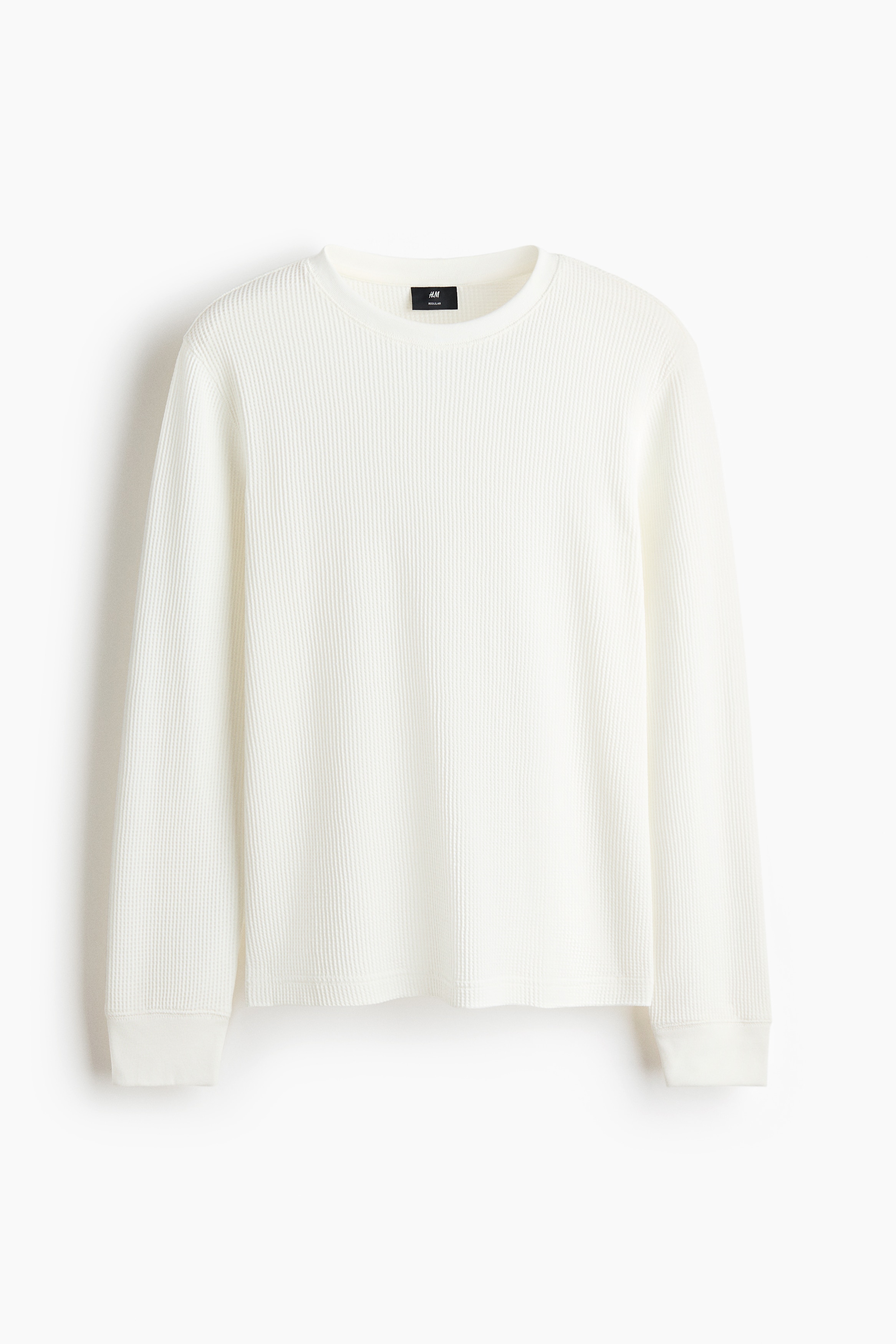 A white long-sleeve tee in a waffled cotton-blend jersey is worn by the model, who is standing with one hand in the pocket of dark brown wide-leg trousers. The tee features a relaxed fit with a ribbed round neckline and ribbed cuffs.