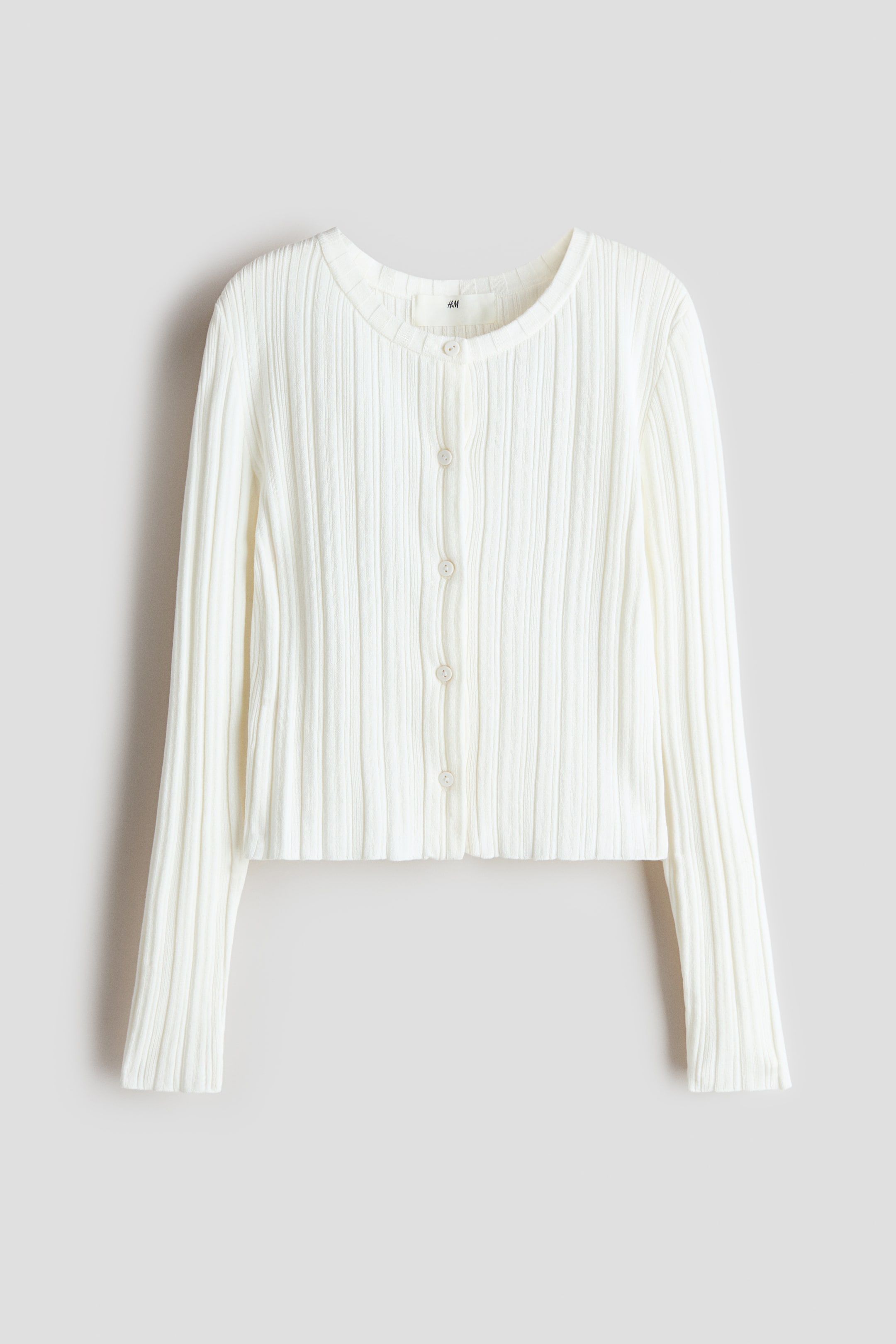 Agrandir l'image: Un cardigan en maille côtelée blanche est présenté de face, avec un col rond et une fermeture à boutons sur le devant avec de petits boutons blancs. Il est conçu avec des manches longues et une longueur raccourcie.