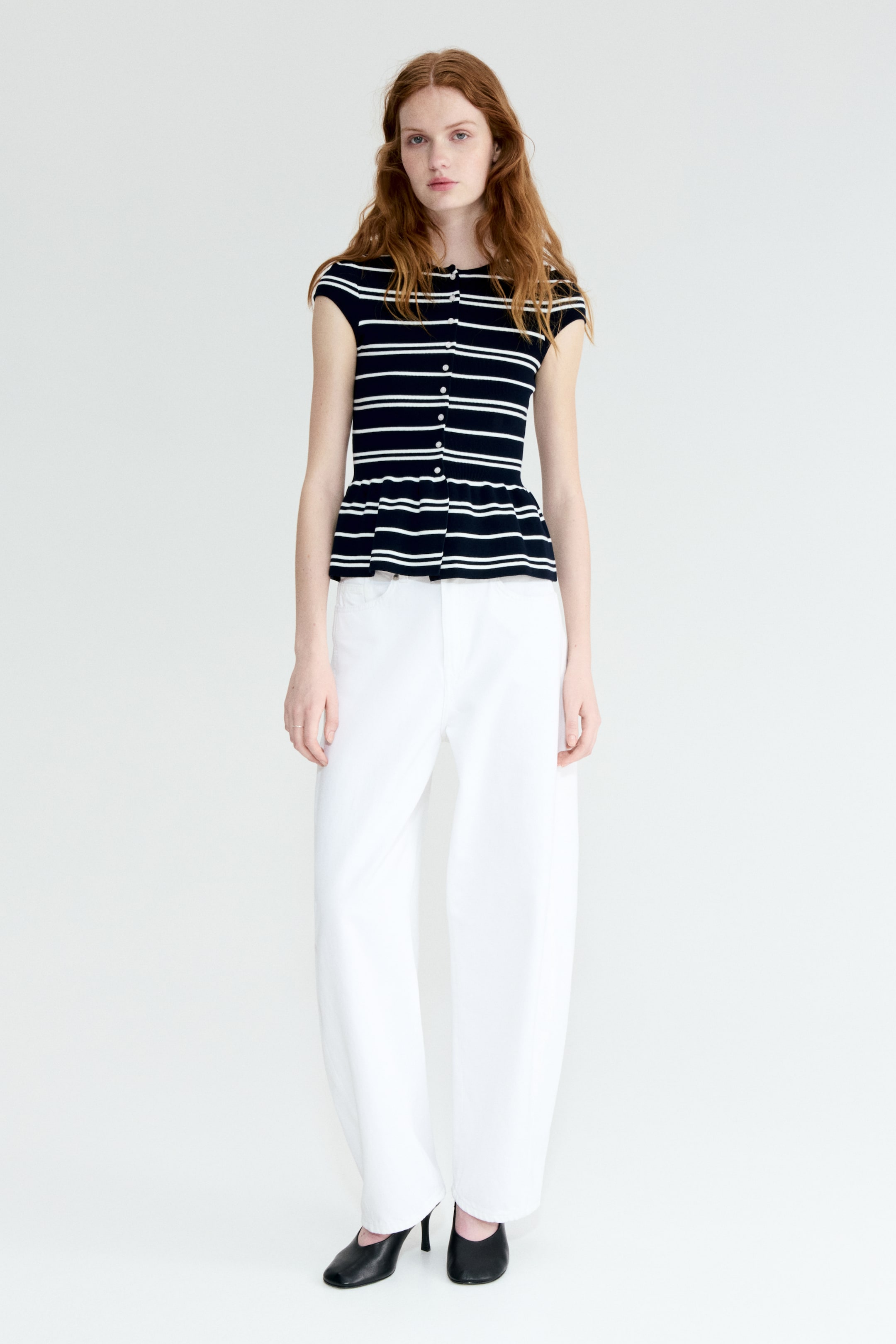 이미지 확대 보기: 검정과 흰색의 가로 줄무늬 니트 상의는 흰색 버튼이 있는 버튼 프론트 클로저, 라운드 넥라인, 짧은 캡 소매, 플레어 페플럼 헴이 특징입니다.