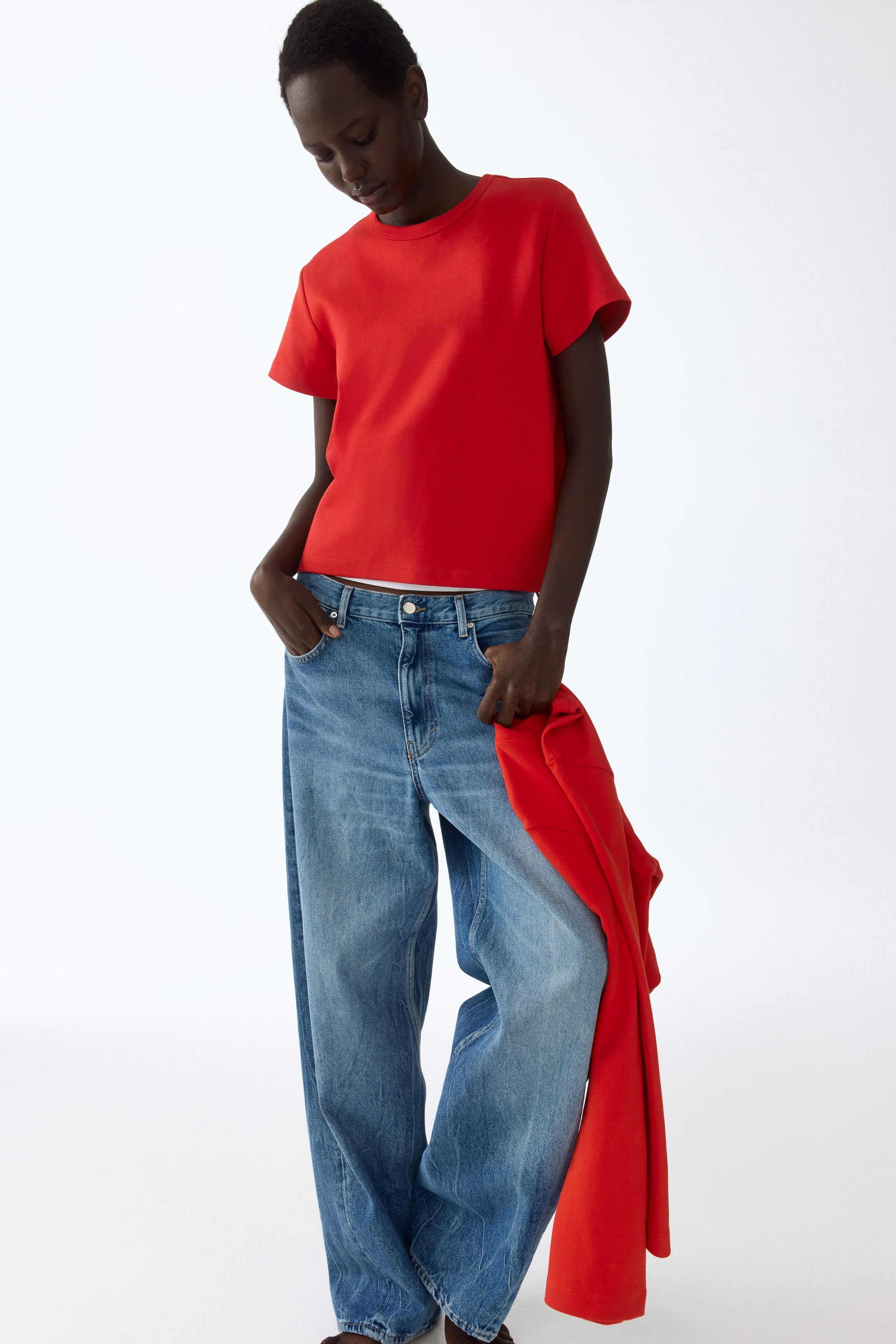 View larger image: A red crew-neck t-shirt with short sleeves and a relaxed fit is paired with blue wide-leg jeans, showcasing a faded wash. A matching red jacket is casually draped over one leg.