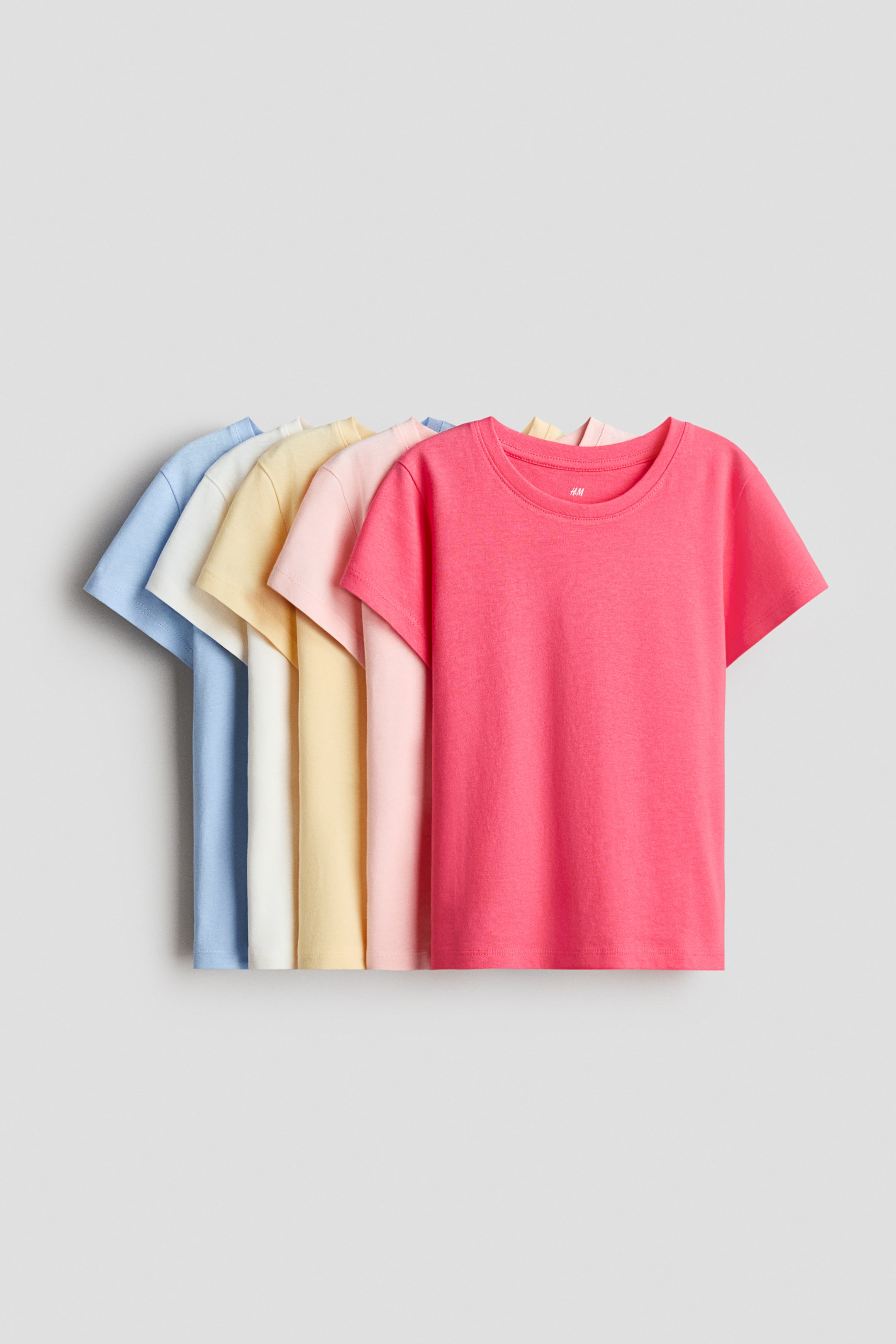 View larger image: Five t-shirts made of soft cotton jersey are arranged in a fan-like display from left to right, showcasing colors in light blue, off-white, yellow, light pink, and pink. Each t-shirt features a round, ribbed neckline and subtly dropped shoulders.