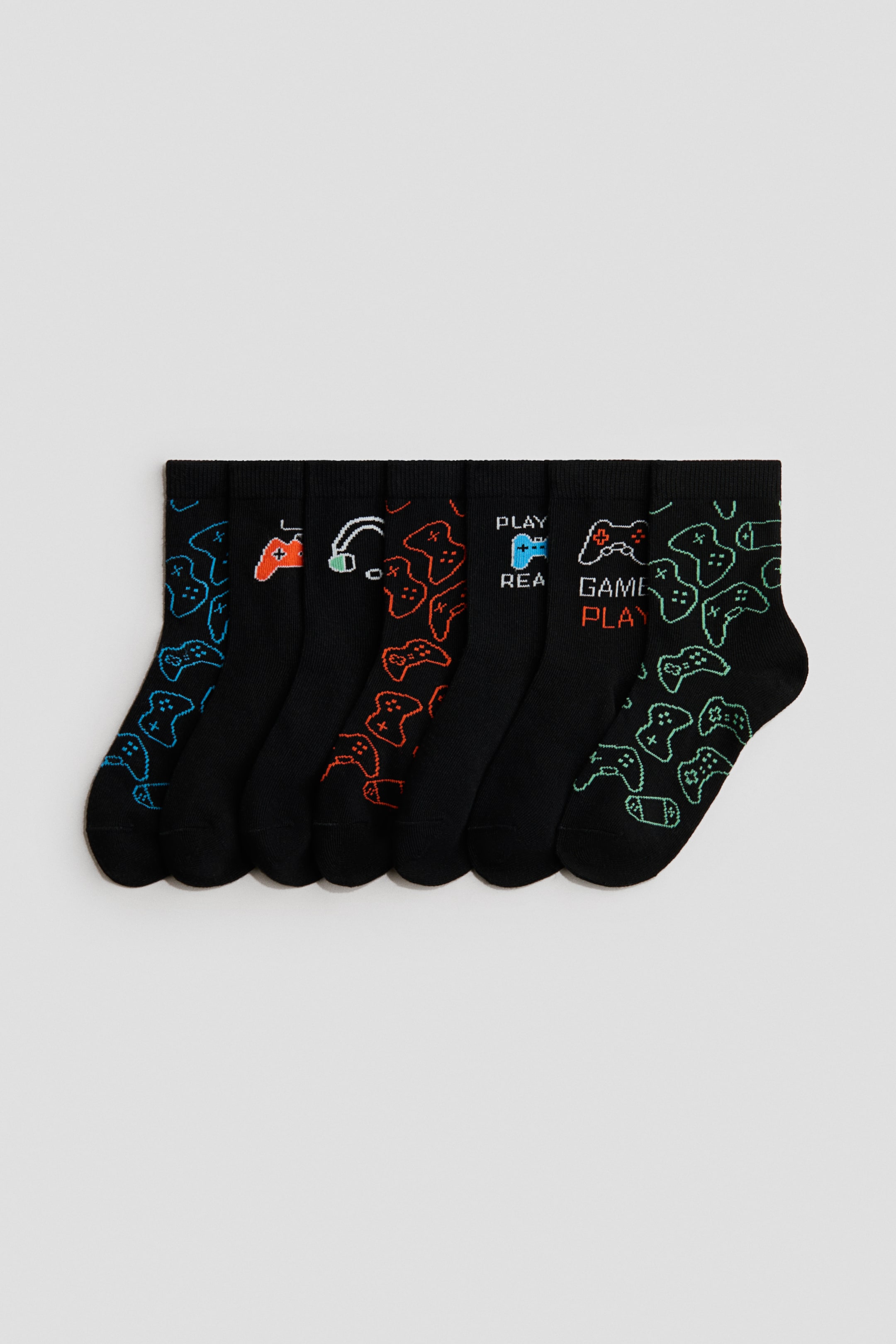 Visa större bild: Sex strumpor visar sina framsidor, tillverkade av en mjuk, finstickad bomullsblandning med elastiska kanter. Varje svart strumpa har olika spelteman med mönster som visar spelkontroller och hörlurar i ljusa blå, orange och gröna färger, och några visar även texten "PLAY" och "GAME PLAY".