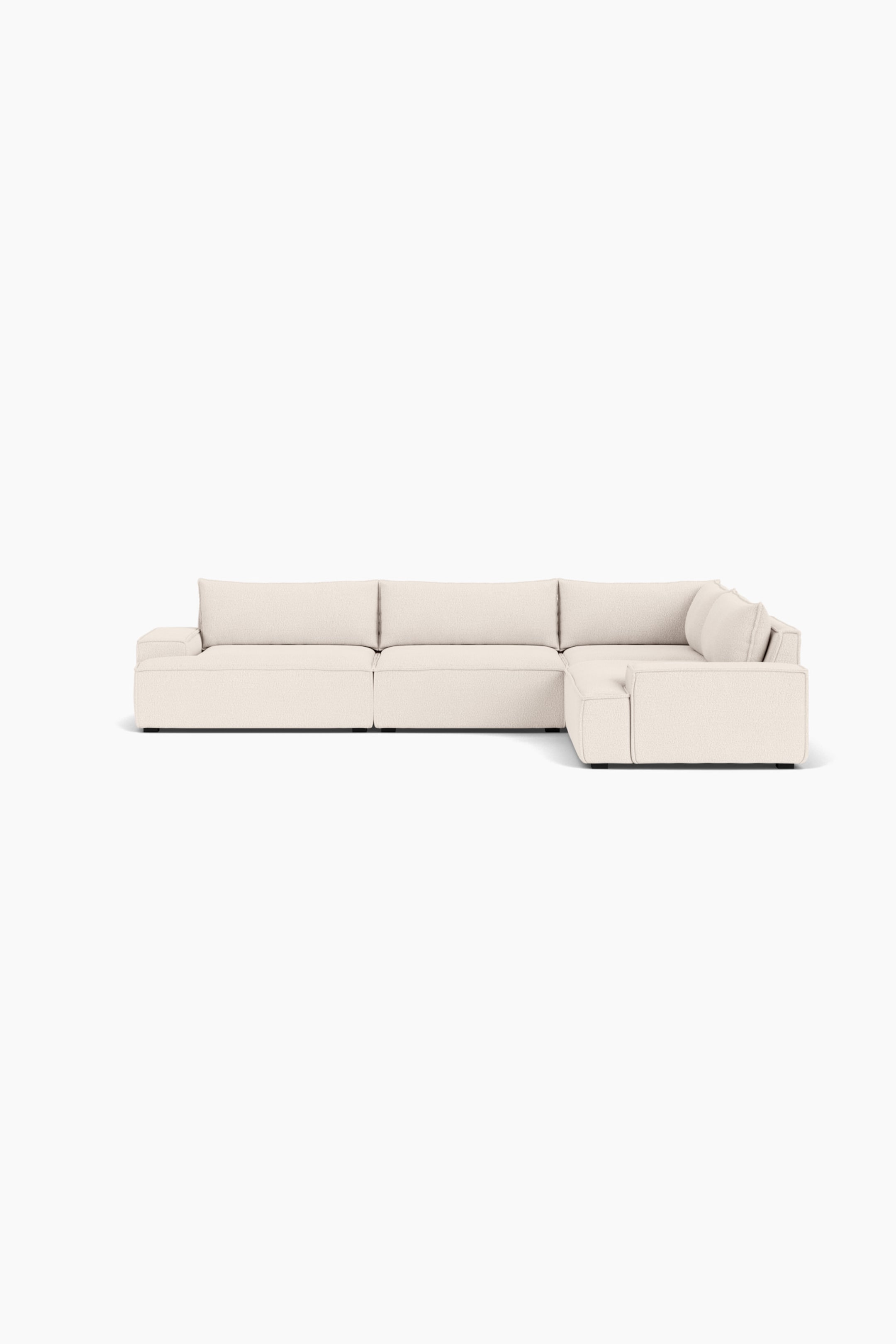 Größeres Bild ansehen: Ein L-förmiges Ecksofa, bezogen mit einem strukturierten cremefarbenen Stoff, ist leicht nach rechts ausgerichtet und präsentiert sein flaches, modulares Design. Es verfügt über tiefe Sitzflächen im Blockstil, breite, quadratische Armlehnen und weiche, lose Rückenkissen.