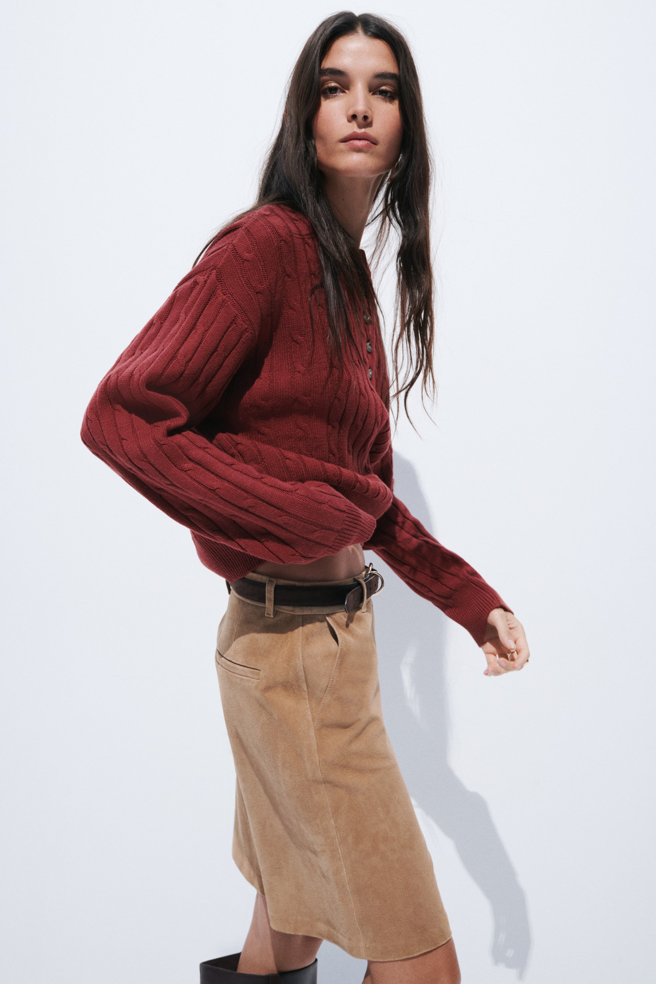 View larger image: A deep red cable-knit jumper, angled to the right, highlights a round neckline with a three-button Henley placket, long sleeves with ribbed cuffs, and a slightly tucked ribbed hem.