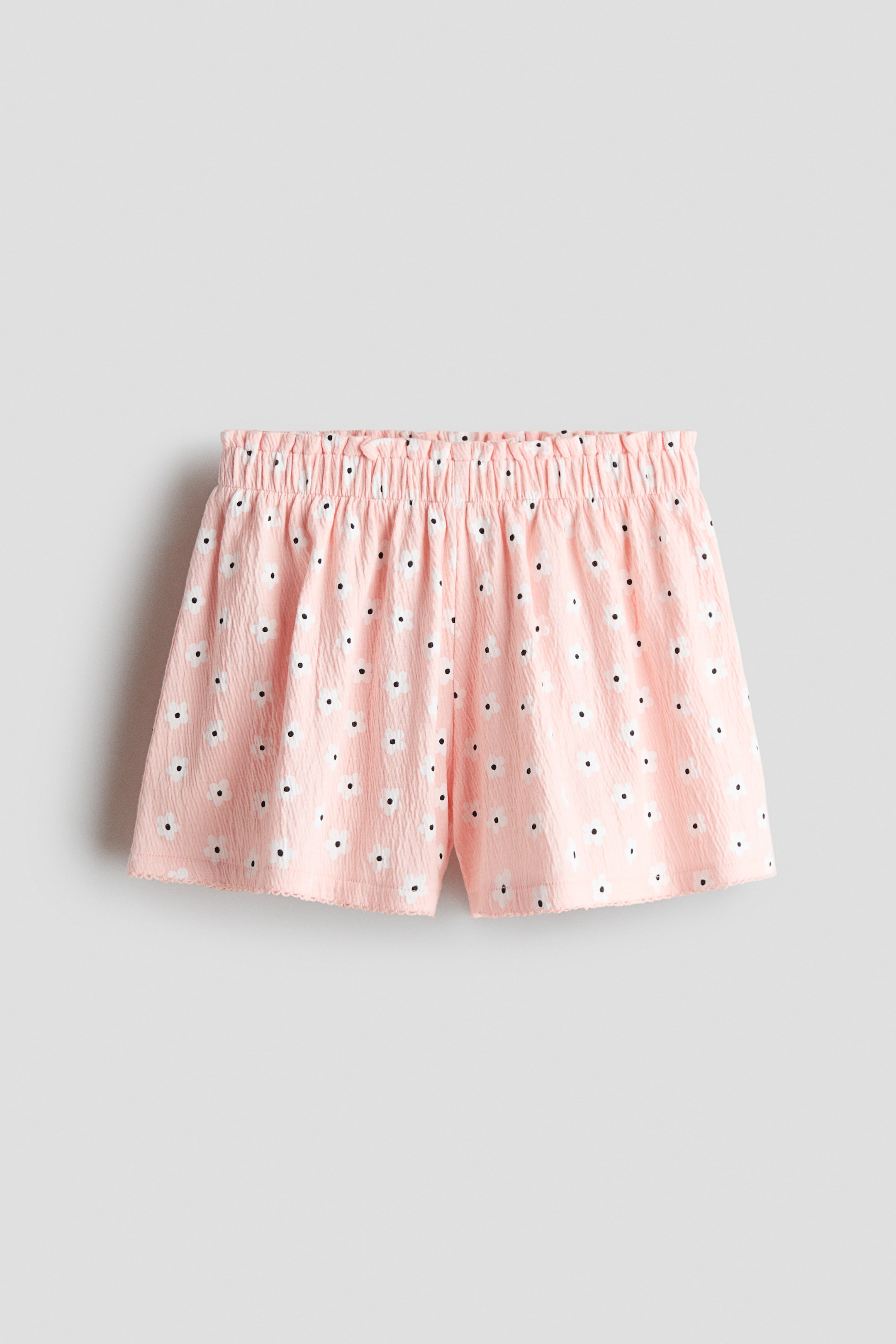 Visa större bild: De framåtvända shortsen har ett mjukt, texturerat rosa bomullsjersey med ett heltäckande vitt blommönster och svarta mittpunkter. De visar upp en elastisk papperspåselinning och picot-kantade fållar.