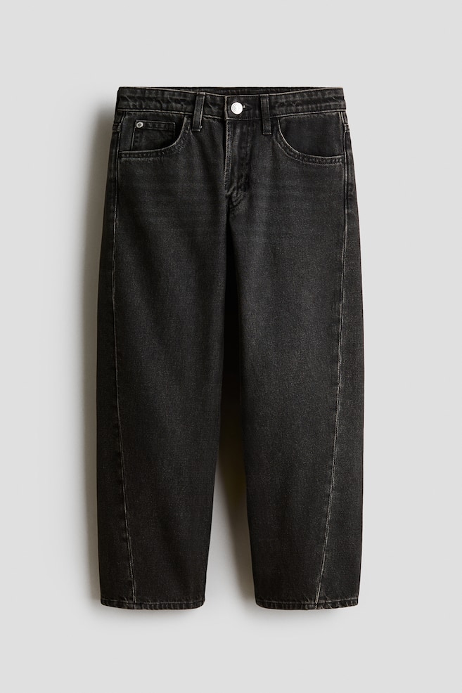 Ett par tvÃ¤ttade svarta denimjeans Ã¤r fotograferade framifrÃ¥n och visar en lÃ¶s passform med raka ben och distinkta vridna sÃ¶mmar som lÃ¶per lÃ¤ngs framsidan av varje ben. Jeansen har en klassisk femficksmodell, bÃ¤lteshÃ¤llor och en metallknÃ¤ppning i midjan. - 1
