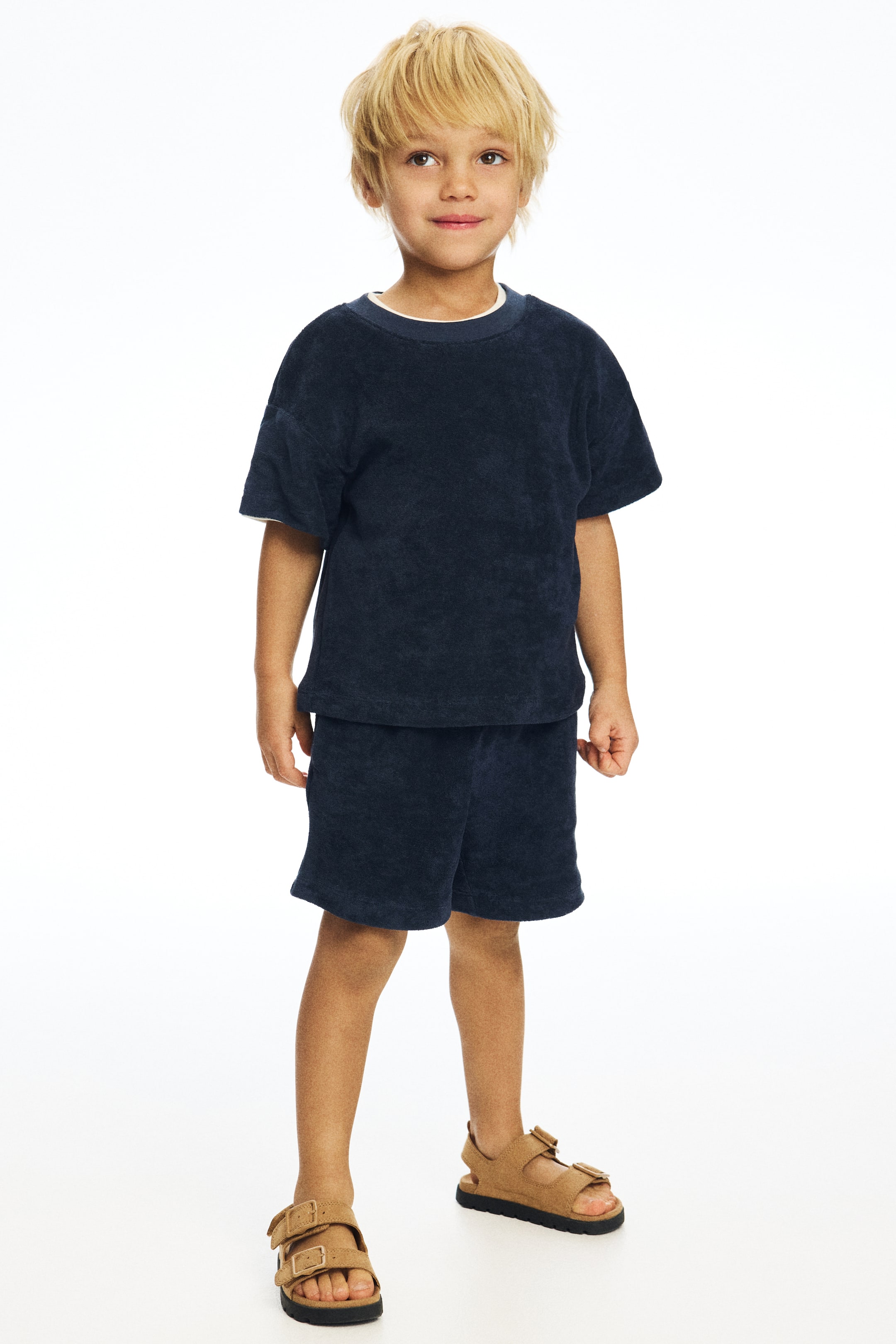 View larger image: A navy blue terry cloth t-shirt and shorts set is being showcased, facing forward. The short-sleeved t-shirt features a crew neck with a visible white lining at the neckline and cuffs, while the matching shorts extend to mid-thigh.