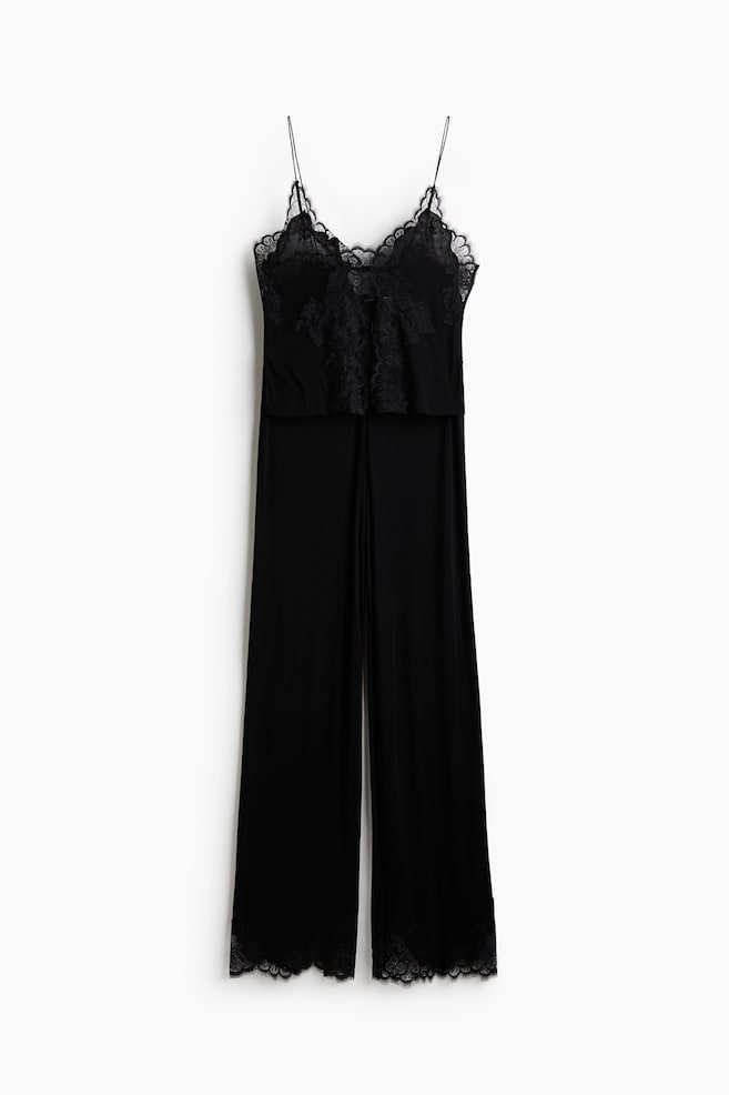 A black jumpsuit is shown from the front, featuring a camisole-style bodice with thin spaghetti straps, a lace-trimmed V-neckline, and delicate lace panelling down the centre. The design includes flowing, wide-leg trousers finished with matching lace trim along the bottom hems. - 1