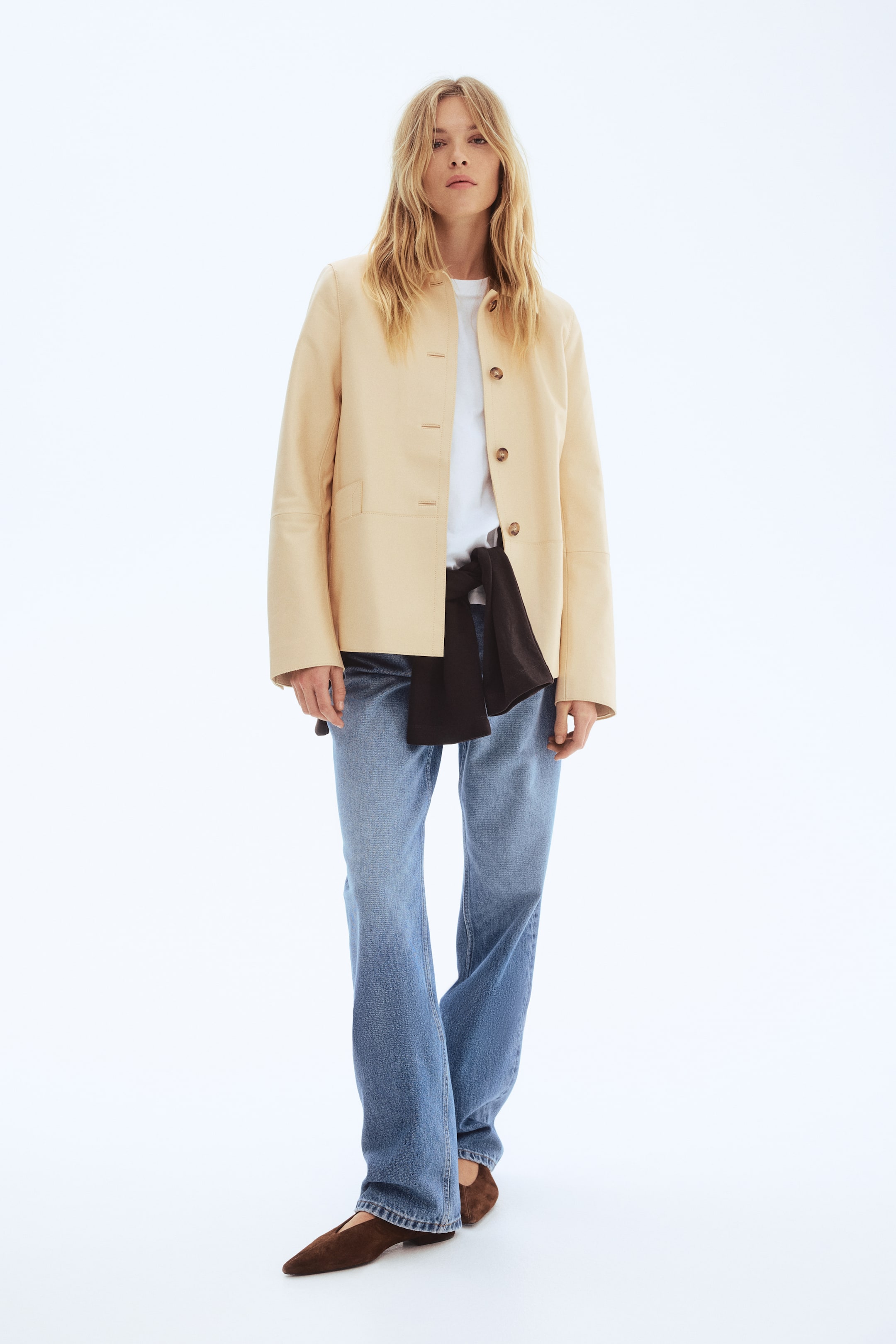 Προβολή μεγαλύτερης εικόνας: Ένα ανοιχτό κίτρινο σακάκι εκτίθεται, με πρόσοψη προς τα εμπρός, παρουσιάζοντας χαλαρή εφαρμογή, λαιμόκοψη χωρίς γιακά, τέσσερα εμφανή καφέ κουμπιά κατά μήκος της μπροστινής πλευράς και δύο μπροστινές τσέπες τύπου patch. Ένα λευκό t-shirt φοριέται από κάτω, ενώ ένα σκούρο ρούχο είναι δεμένο γύρω από τη μέση.