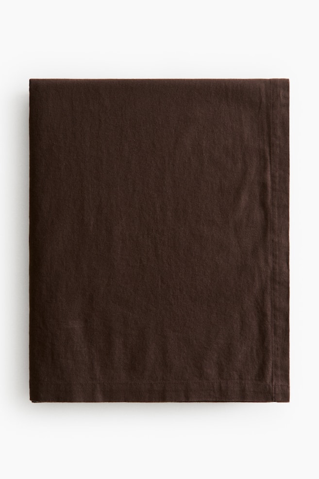 A dark brown cotton and linen blend tablecloth is lying folded flat in a front-facing view, displaying its textured weave and a wide folded hem along the edges. - 1