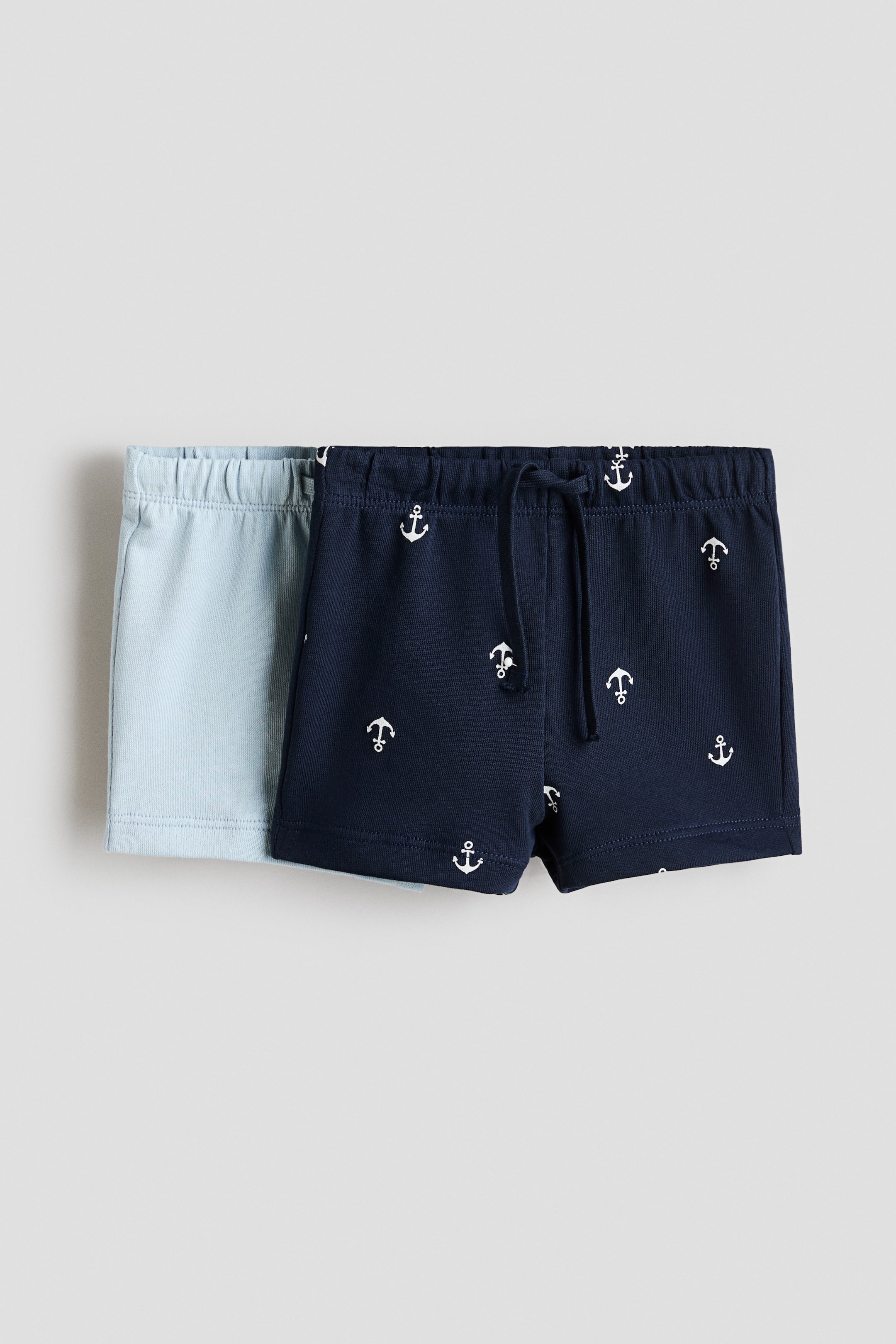 Ver imagen más grande: Se presentan dos pares de pantalones cortos para bebé, con un par liso de color azul claro colocado detrás de un par de color azul marino. Los pantalones cortos azul marino, orientados hacia el FRENTE, presentan un diseño de anclas blancas y una cintura elástica con cordón ajustable.
