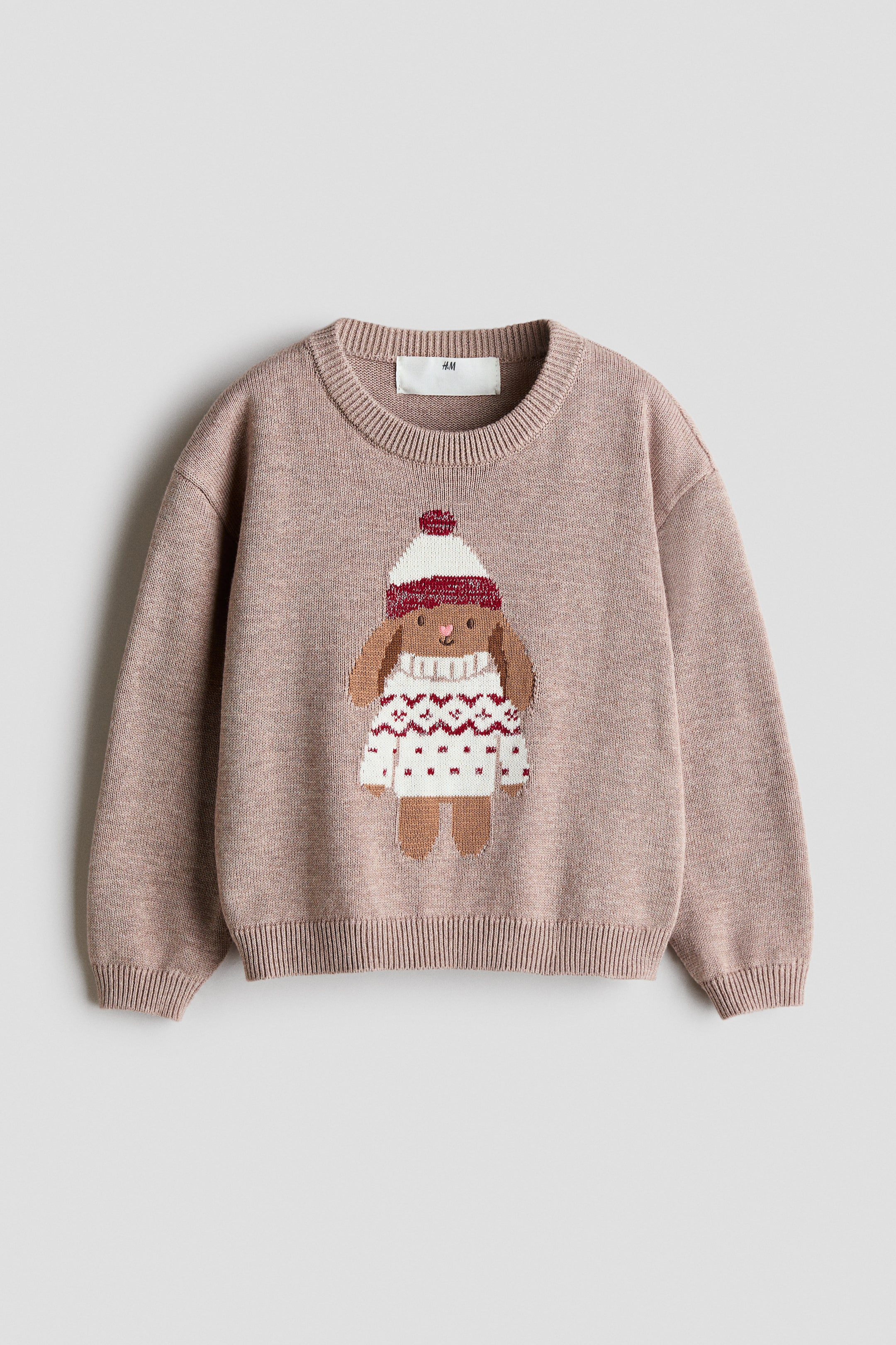 Agrandir l'image: Un pull en coton tricoté jacquard rose poudré est présenté de face, mettant en valeur un motif tricoté central représentant un chien portant un bonnet d’hiver et un pull. Le pull présente un col rond bordé de côtes, des épaules tombantes, des manches longues et des finitions côtelées aux poignets et à l’ourlet.