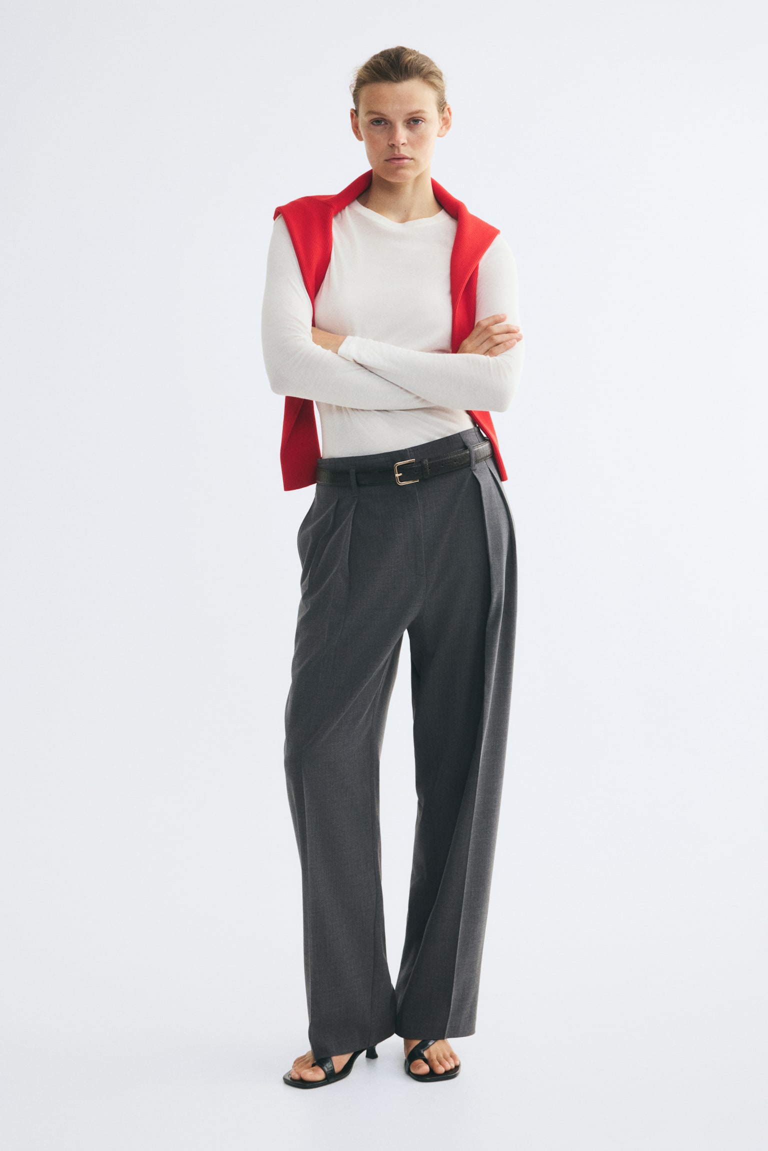 Dark grey pleated trousers present a structured waistband with belt loops, through which a dark brown crocodile-embossed belt with a brass buckle is threaded. The trousers feature double front pleats and wide legs with sharp vertical creases. - 1