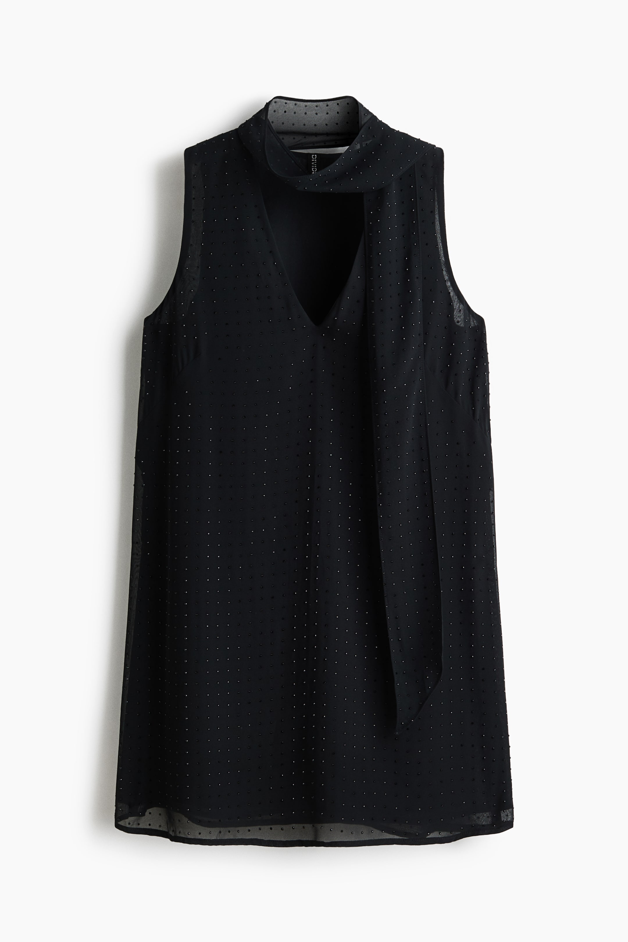 Ampliar la imagen: FRONTAL. Un top negro sin mangas presenta un cuello alto con un corte en V y una corbata integrada en el cuello. La tela transparente muestra una sutil textura de puntos en toda su superficie.