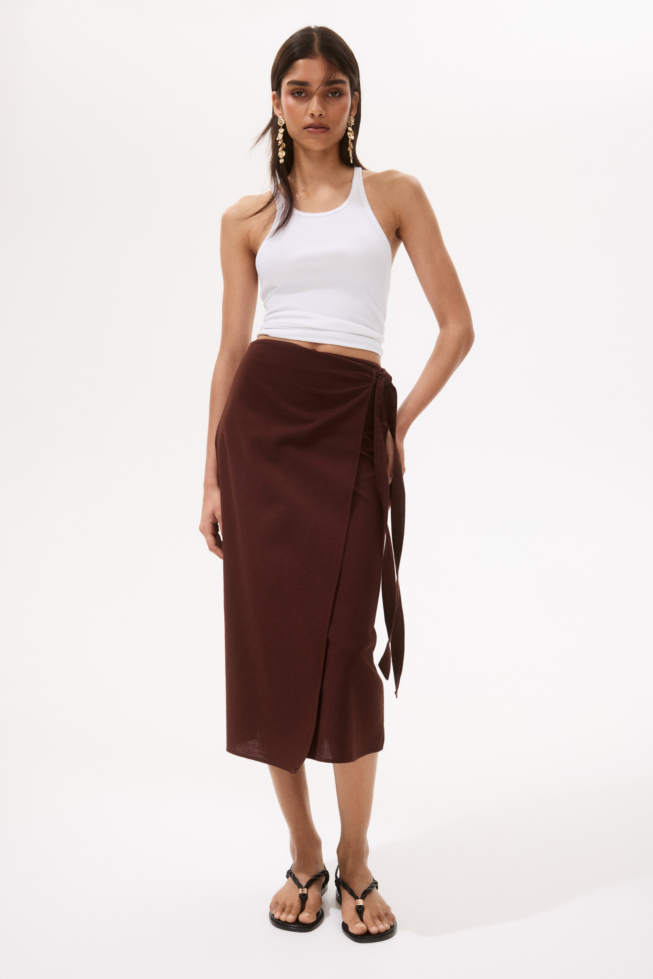 View larger image: A white cropped racerback tank top is being worn. A dark brown midi wrap skirt is tying at the left hip, forming an overlapping front panel.